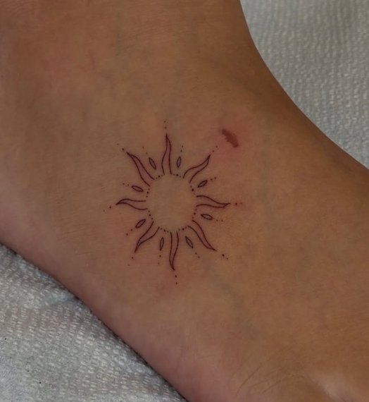 Small sun-shaped tattoo with a sunburst design on the ankle.