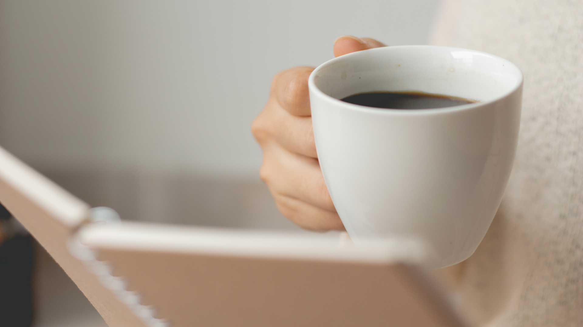 Person holding a white mug filled with black coffee in their left hand, partially visible.