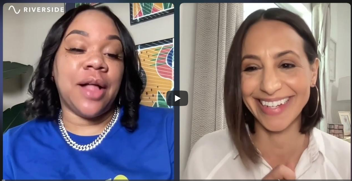 Two women engaged in a video call, one wearing a blue shirt and a silver chain, and the other wearing a white shirt and hoop earrings, smiling at the camera with a colorful background and beige curtains behind her.