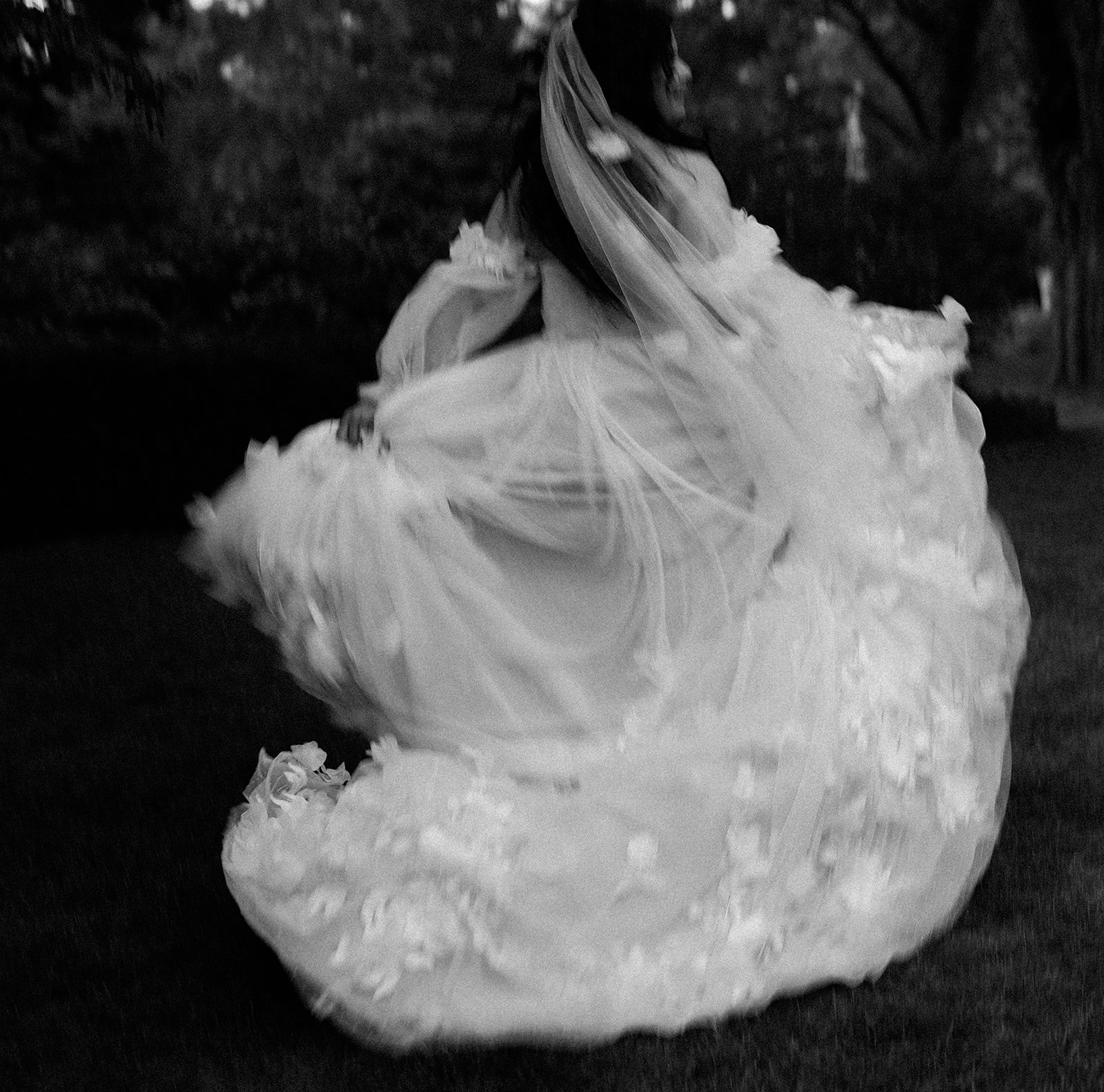 A blurry wedding photograph of a bride with a floral dress and veil running away. The photograph is taken at Long Hill Estate in Beverly, MA by Christina Richards.