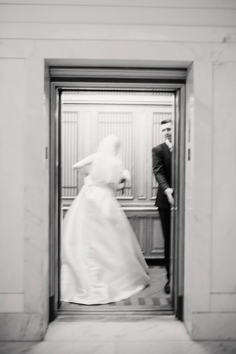 A blurry, black and white documentary wedding photograph of a couple getting into a vintage elevator at San Francisco City Hall.