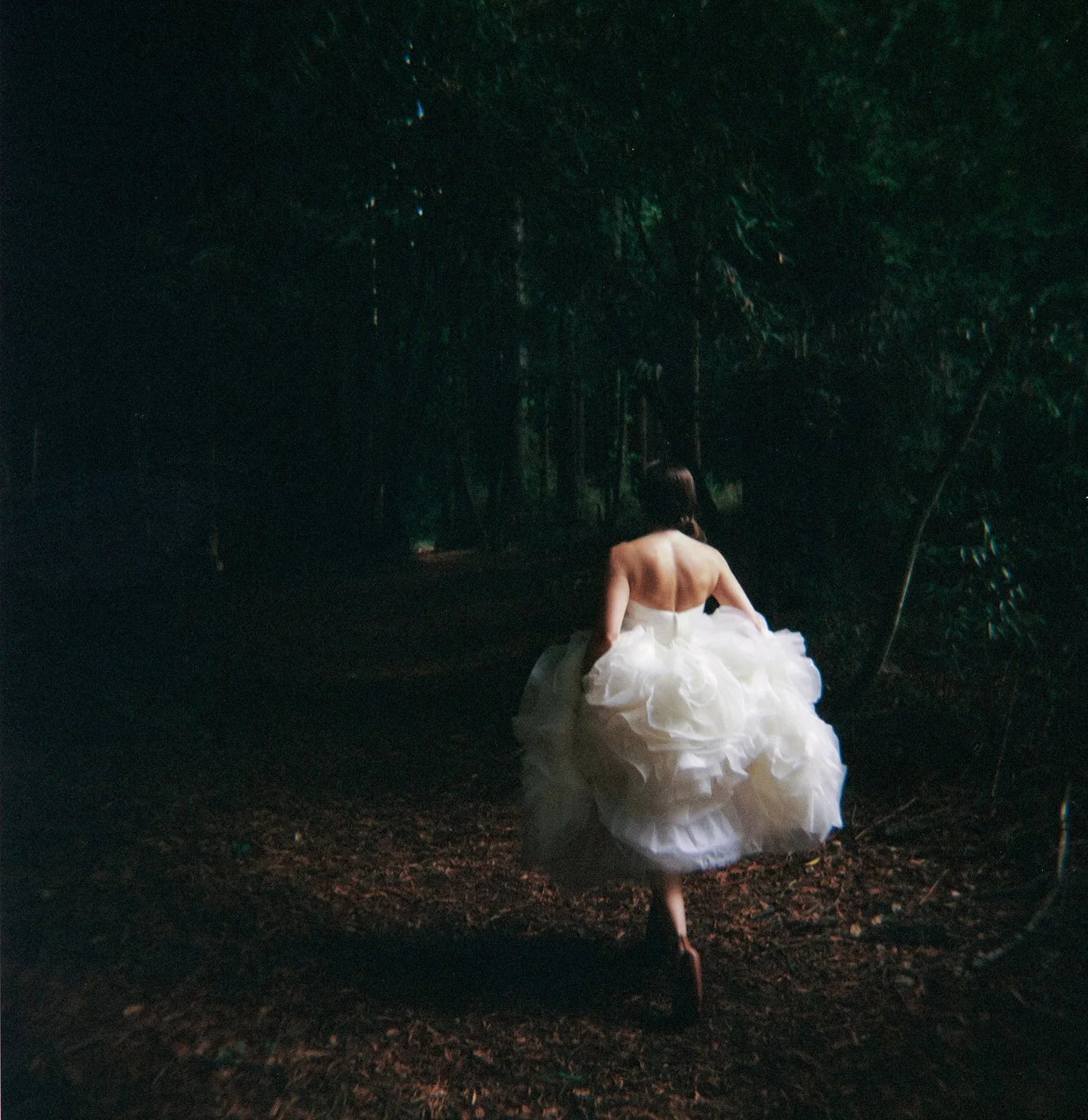 A moody color film photograph of a bride in a forest. The white dress is illuminated by soft light. Photography by Boston based Christina Richards.