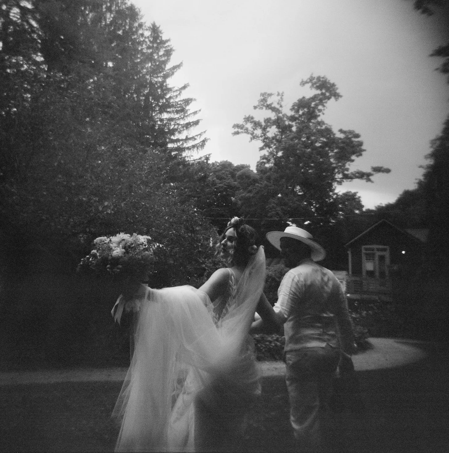 A black and white film photograph of a bride and groom leaving their outdoor wedding ceremony at Race Brook Lodge in Western MA. The photo is soft and candid in feeling.