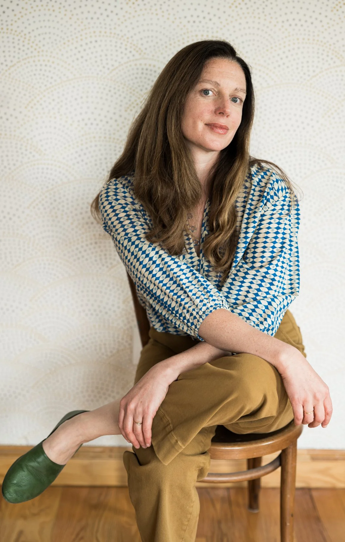 A portrait of fine art, documentary film photographer Christina Richards. The subject is seated on a wood bistro chair looking at the camera.