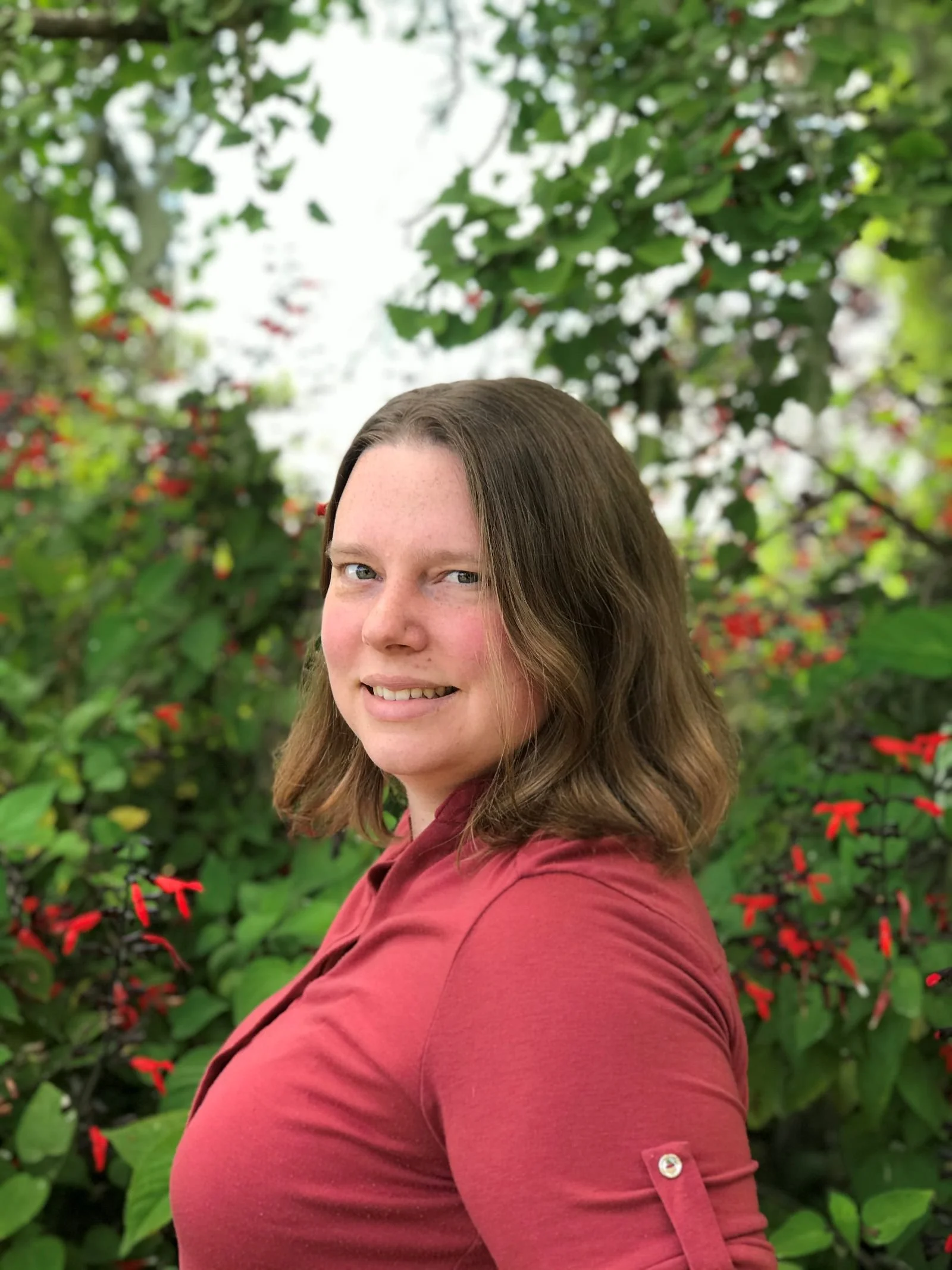 Jessica Brohmer LMFT online therapist for anxiety, grief, trauma, and perfectionism. She is standing in a side profile looking at the camera with a soft smile. She is standing in front of a flowering bush.