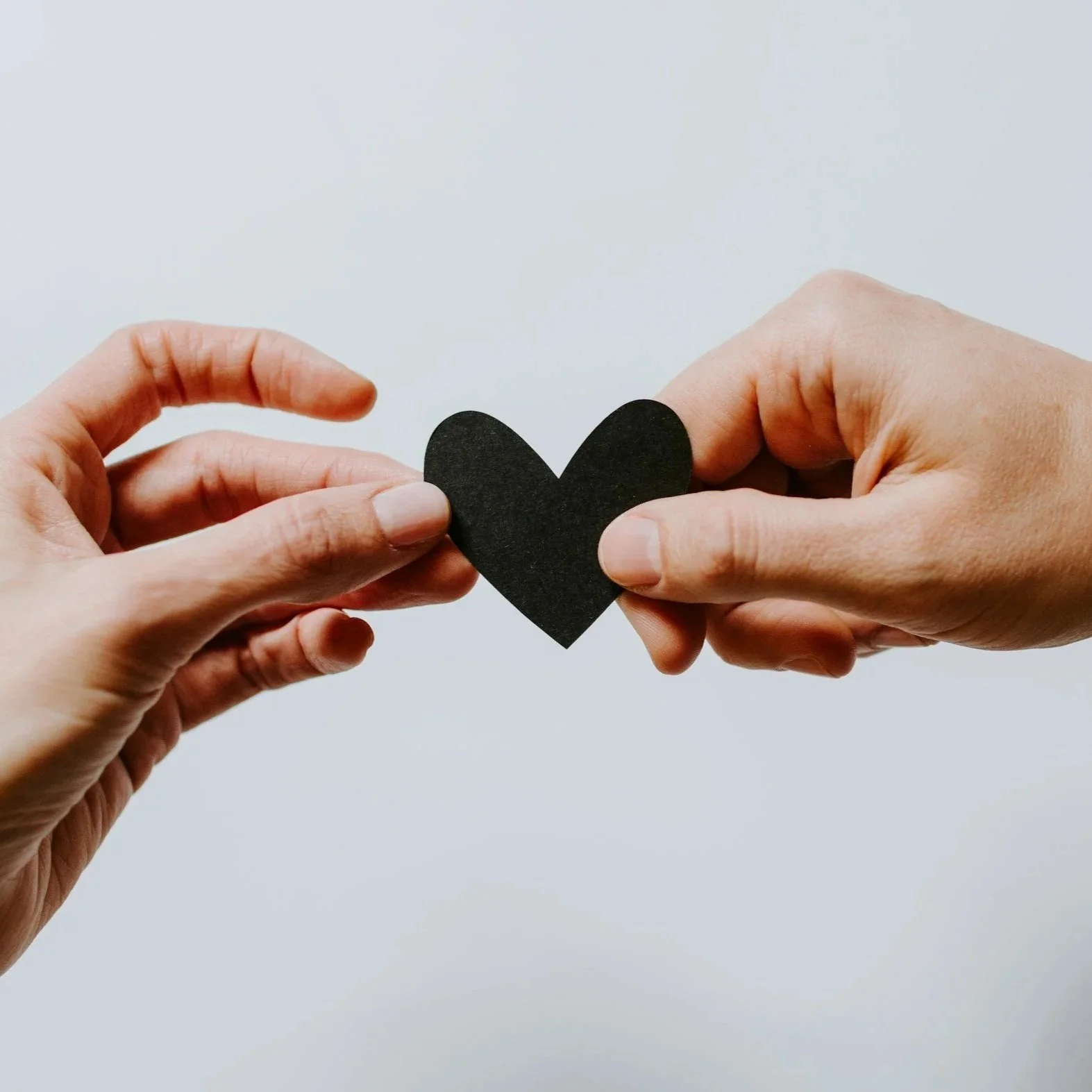 Two hands holding a paper heart against a plain background.