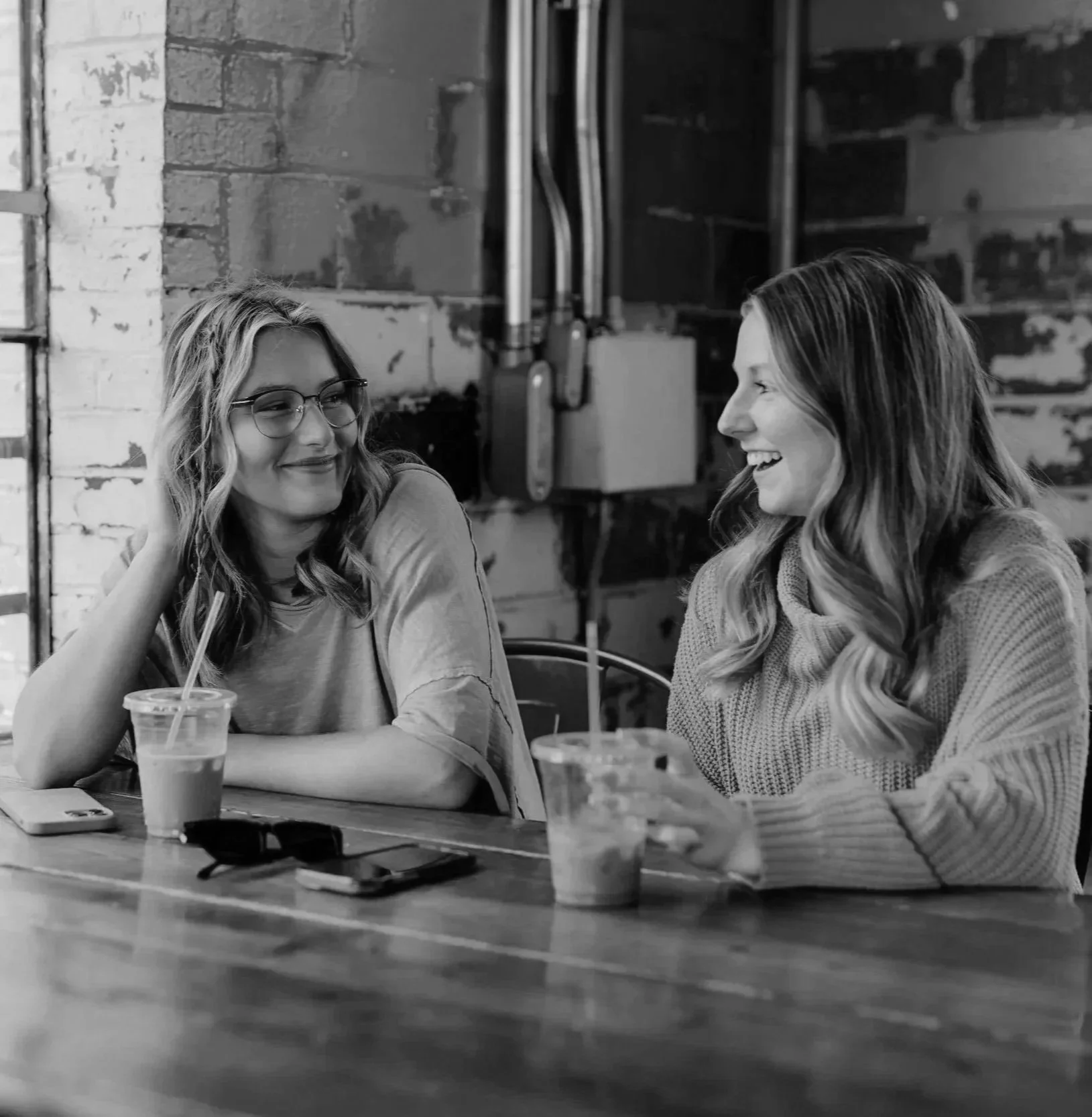 Two women sitting at a table in a cafe, smiling and engaging in conversation.