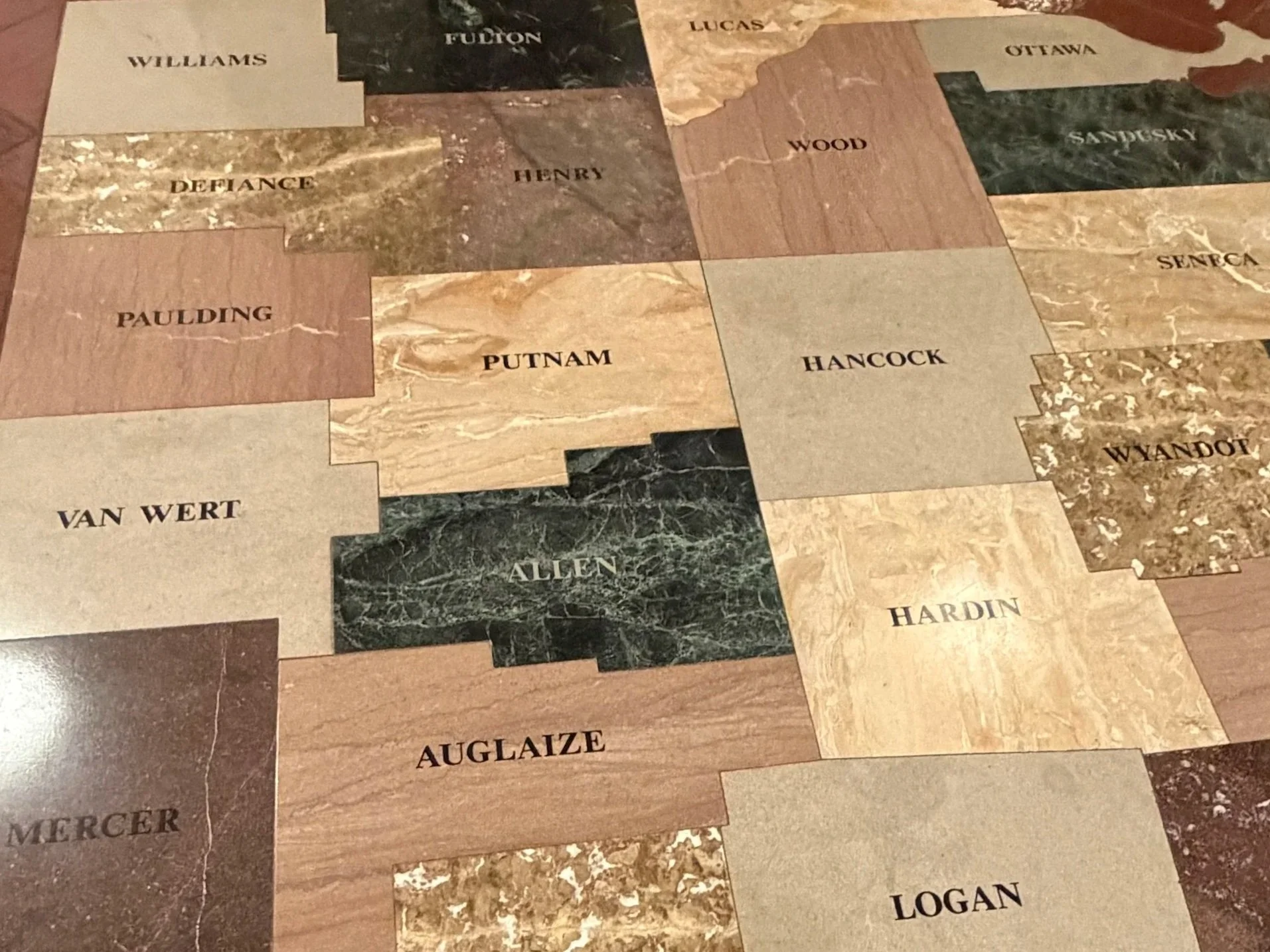 A mosaic of an Ohio county map with various types of marble and stone tiles with names of the NWOCA counties