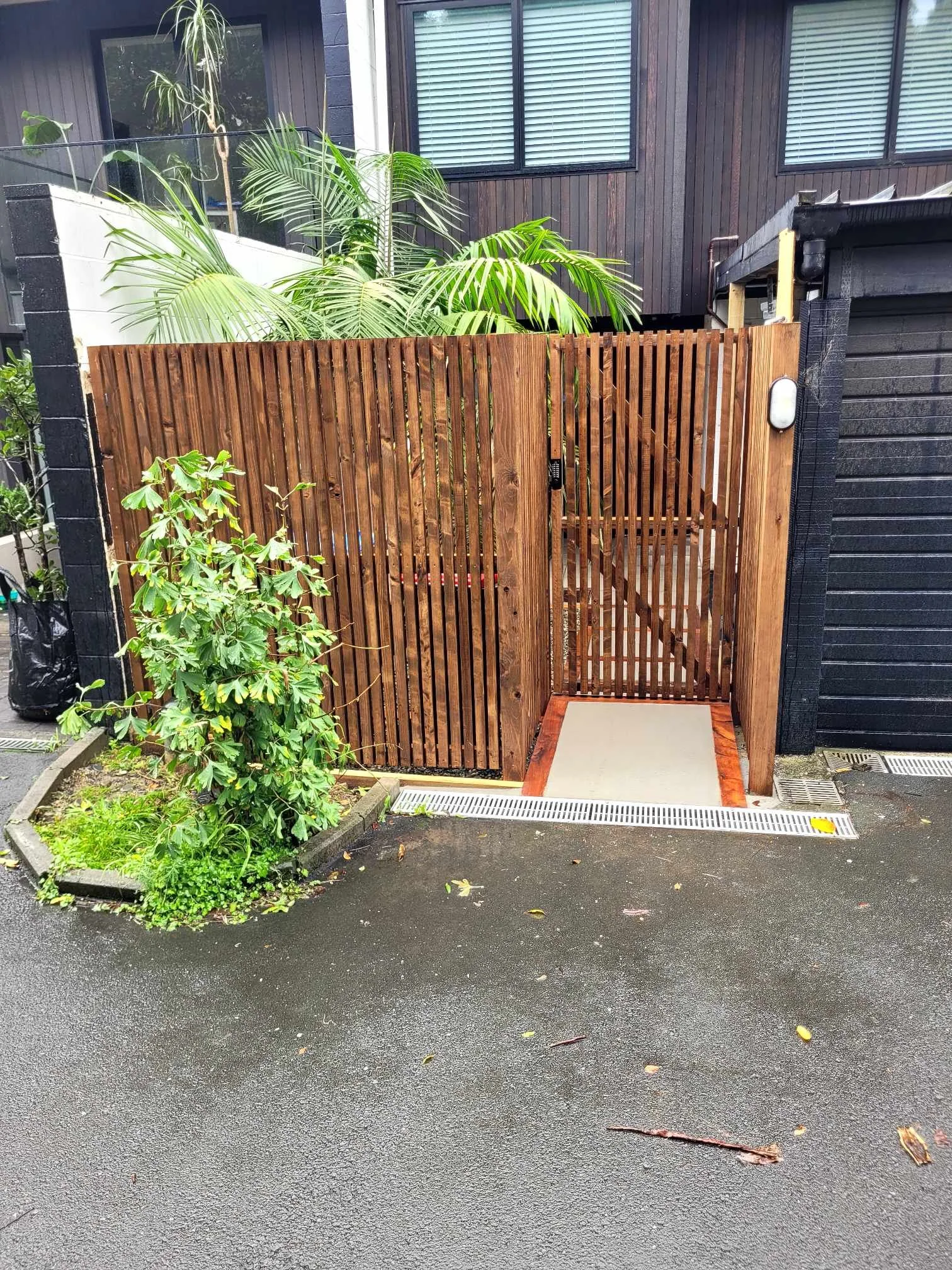 A Cedar vertical fence with a matching gate, featuring steps framed with rich macrocarpa sleepers and finished with smooth concrete, guiding visitors naturally into the property.