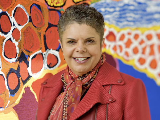 Deborah Cheetham standing in front of the Dulka Warngiid (Land of All) tapestry at the Melbourne Recital Centre