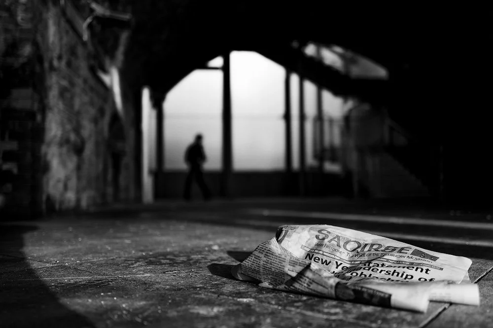 A crumpled newspaper lying on the ground in a shadowy Dublin alleyway, street photography Dublin City Centre.