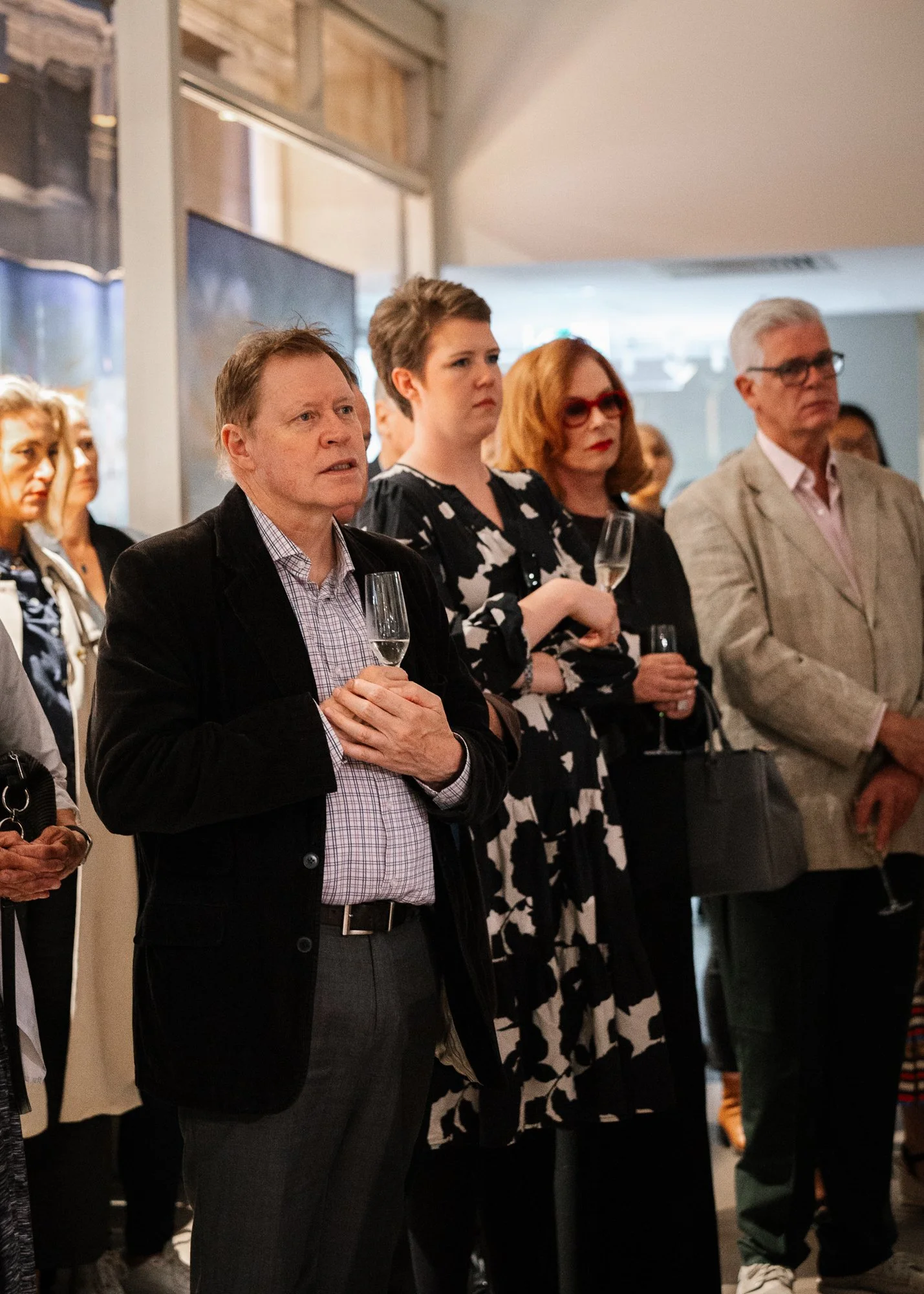 A group of people at a social event, holding wine glasses, listening attentively.
