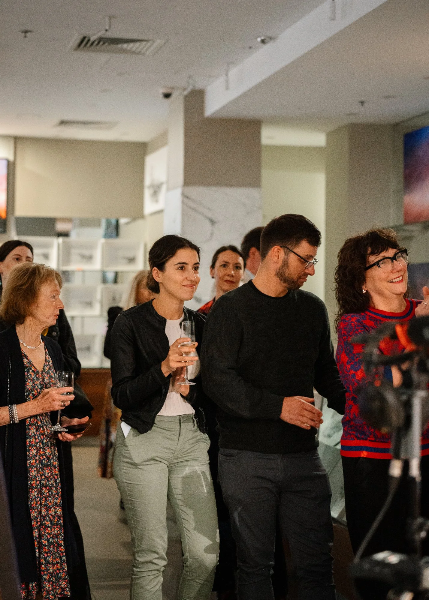 Group of people at a social event, some holding glasses of wine, indoors