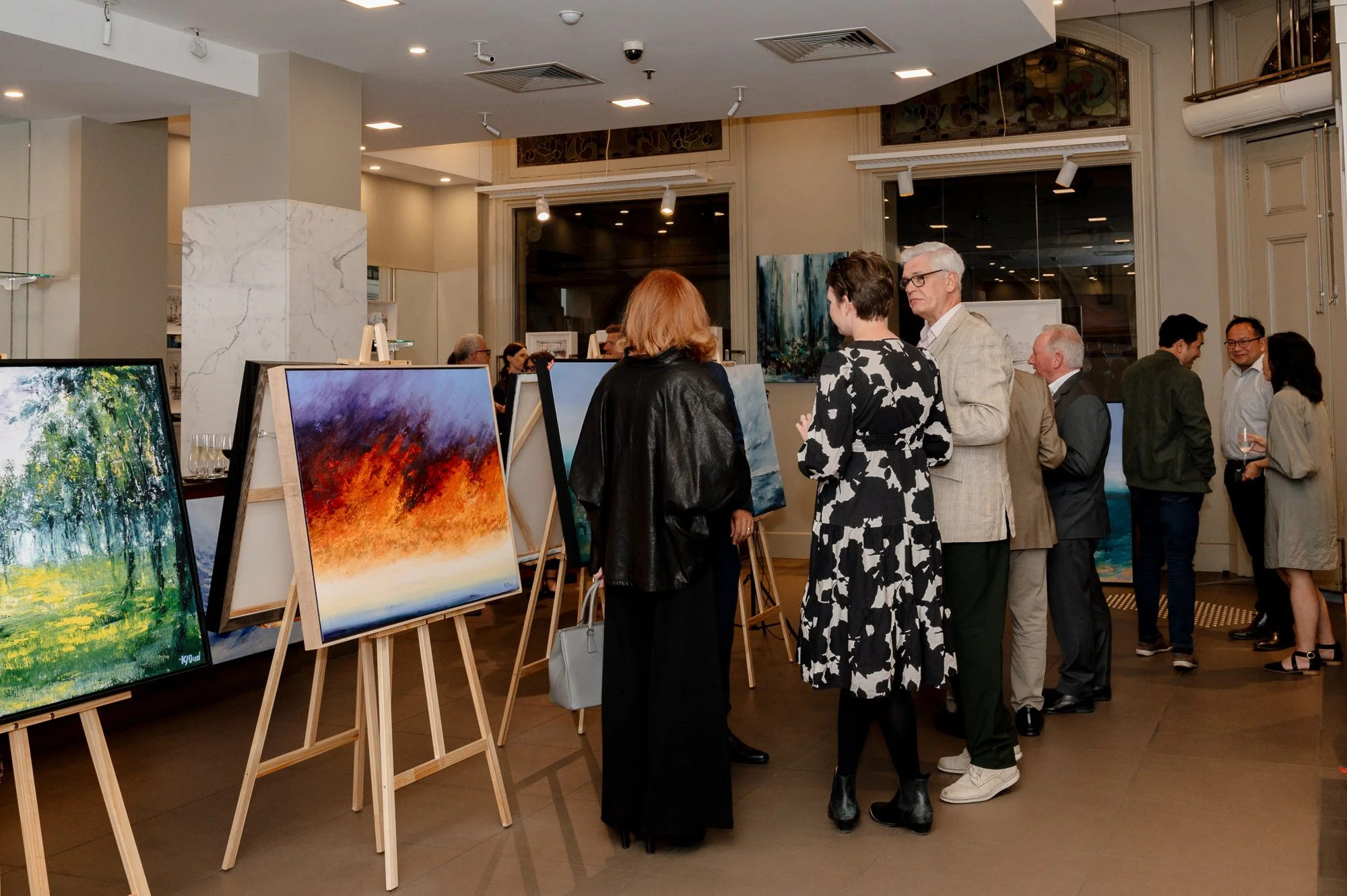 People viewing and discussing colorful paintings at an art gallery exhibition.