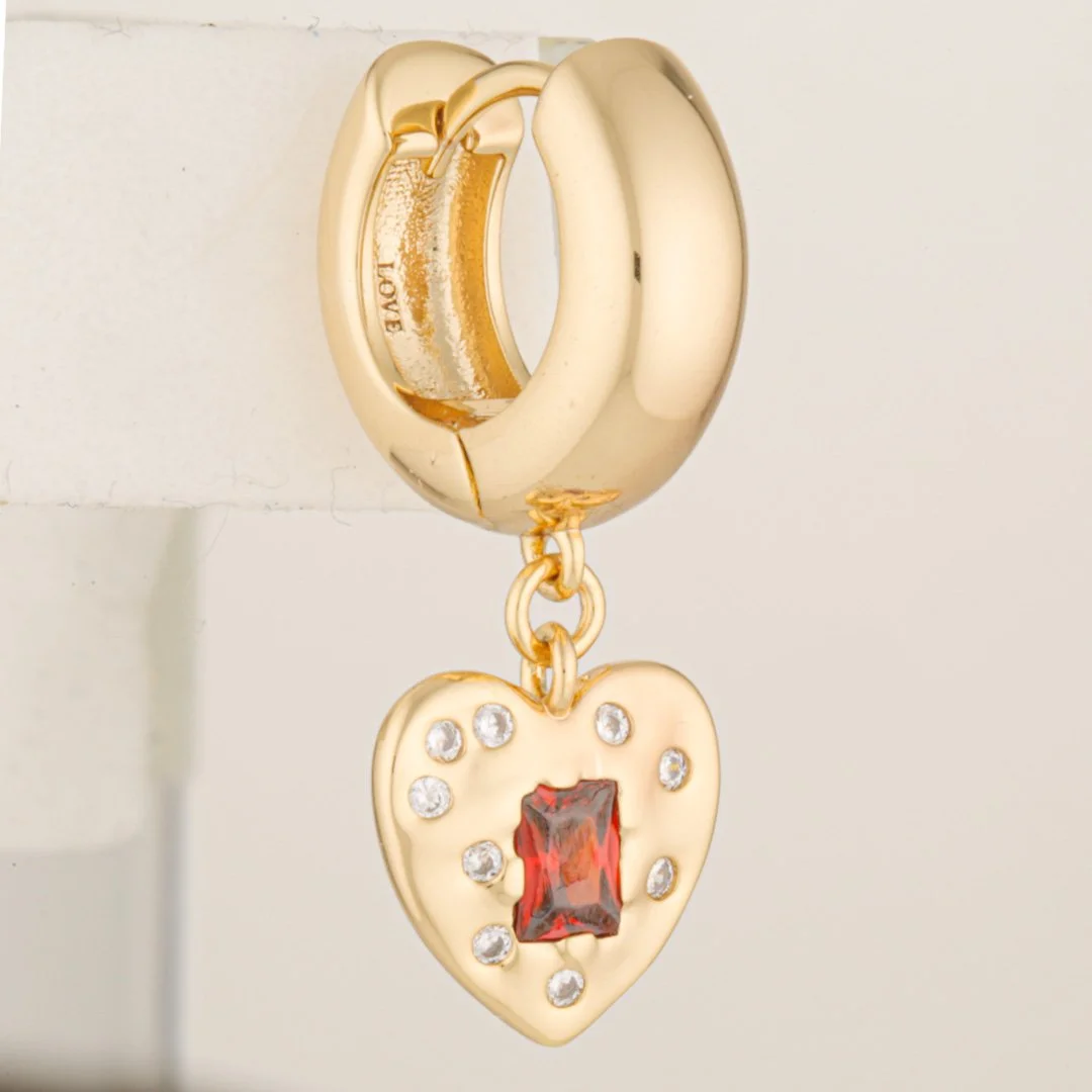 Original studio photograph showing the gold hoop earring with the heart-shaped pendant, red gemstone and white supporting material.