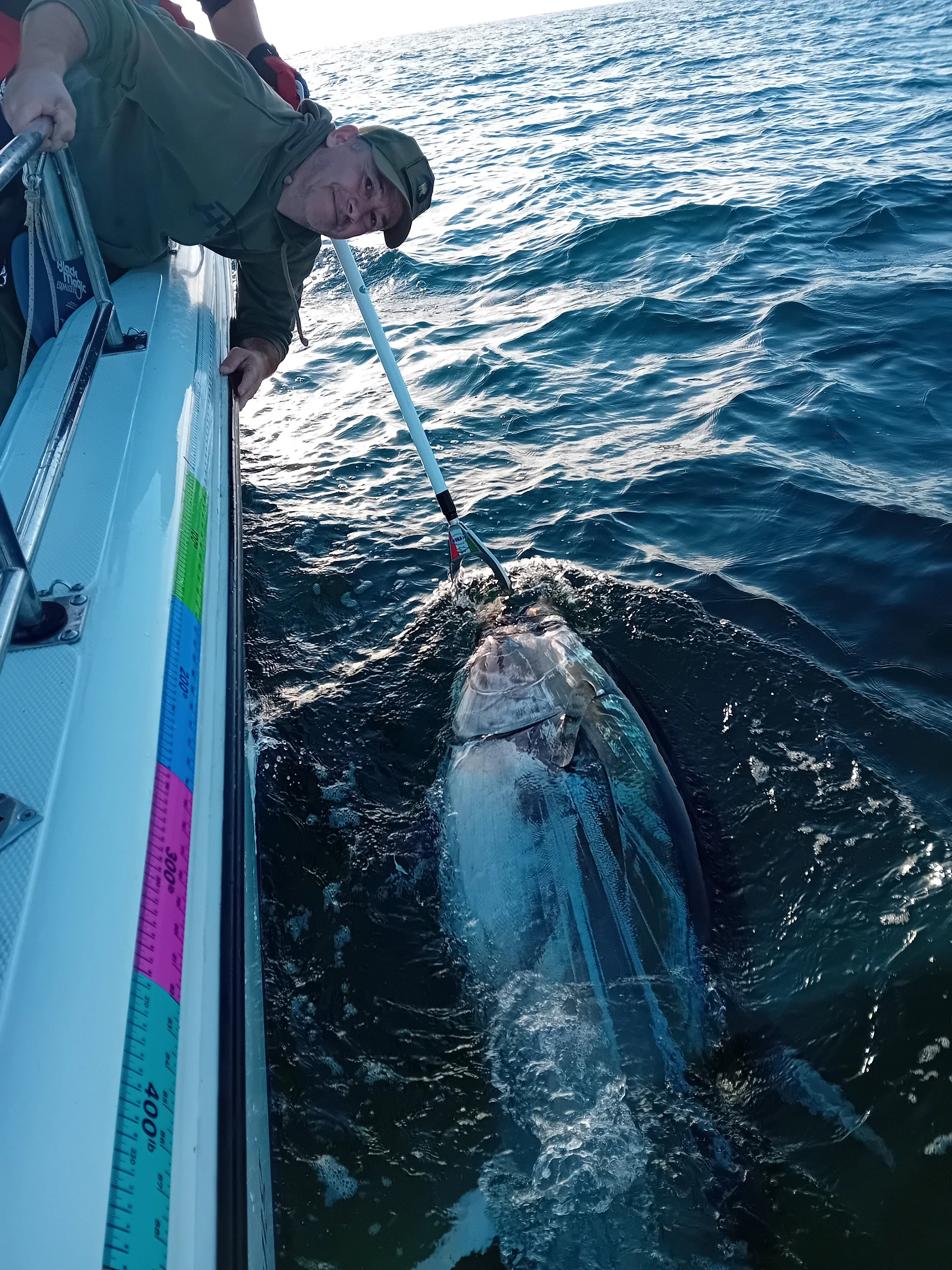A man on a boat using a pole to catch a large fish in the ocean.
