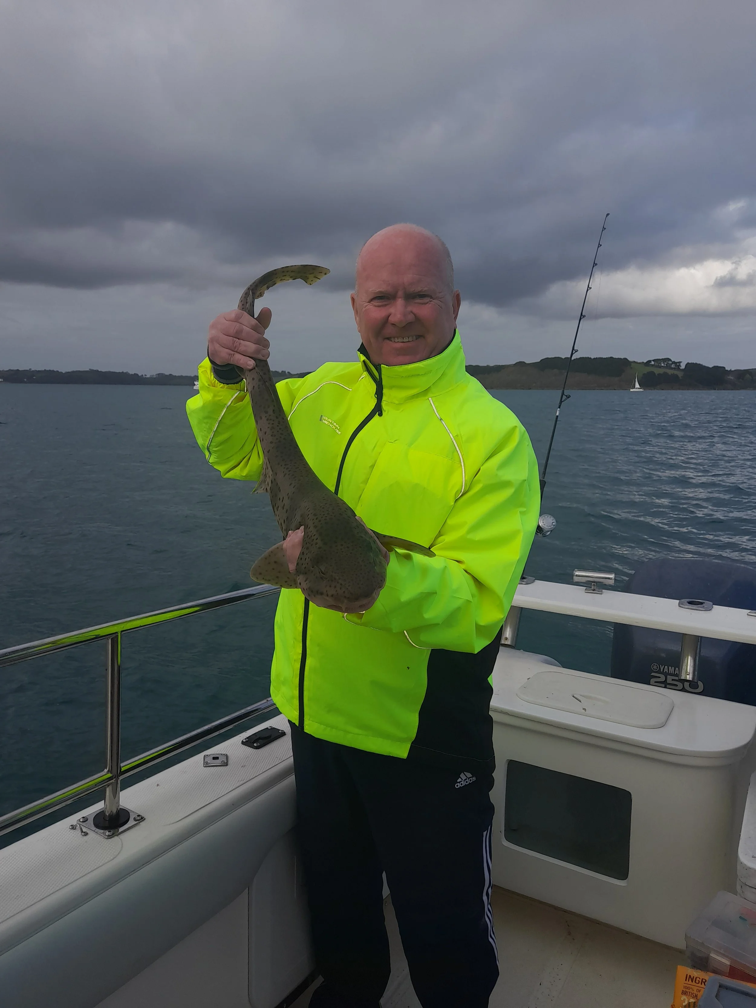 A man in a bright yellow rain jacket holding a fish on a boat during overcast weather.