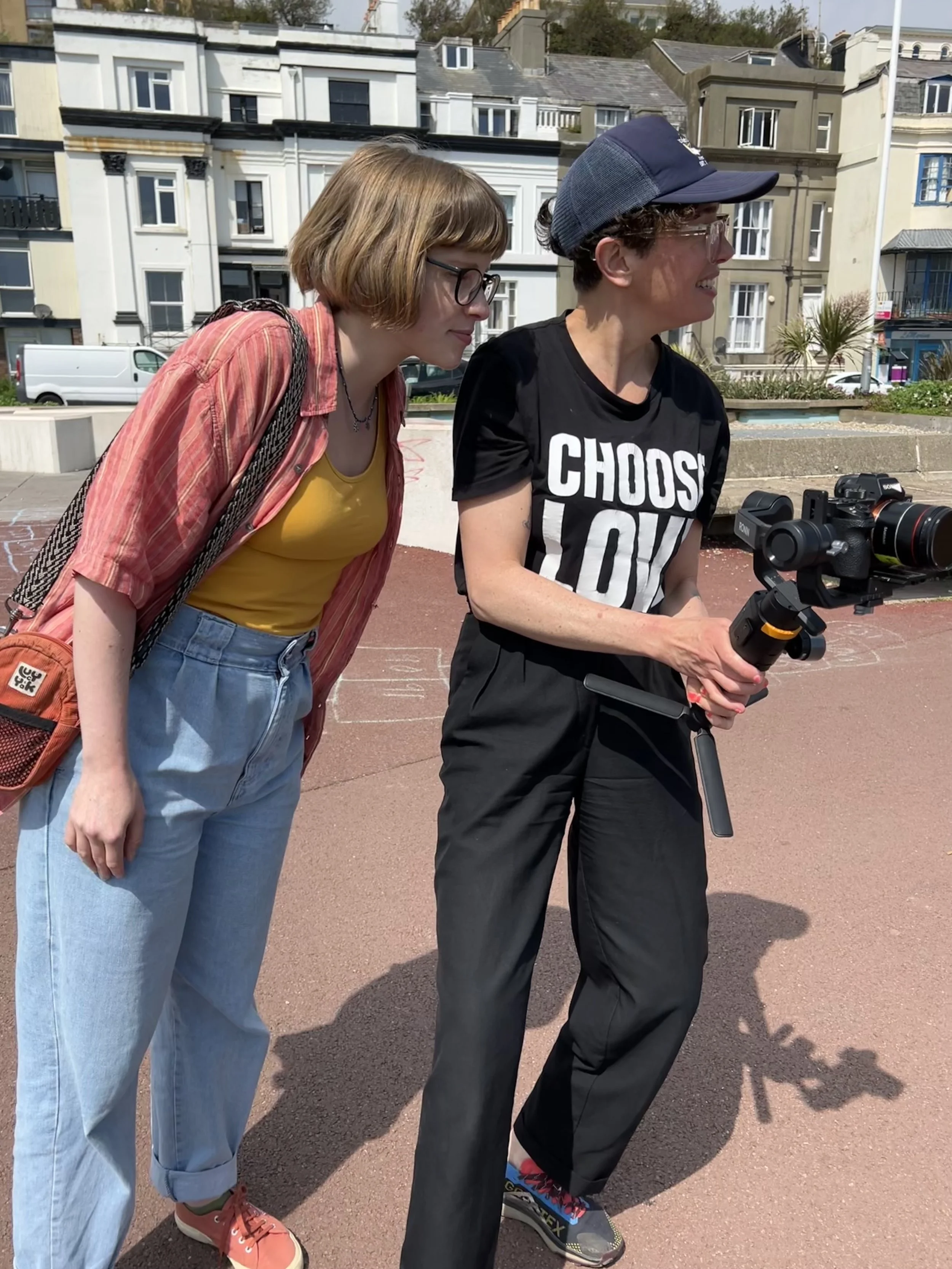 Esther is standing next to a young man holding a camera and looking over his shoulder