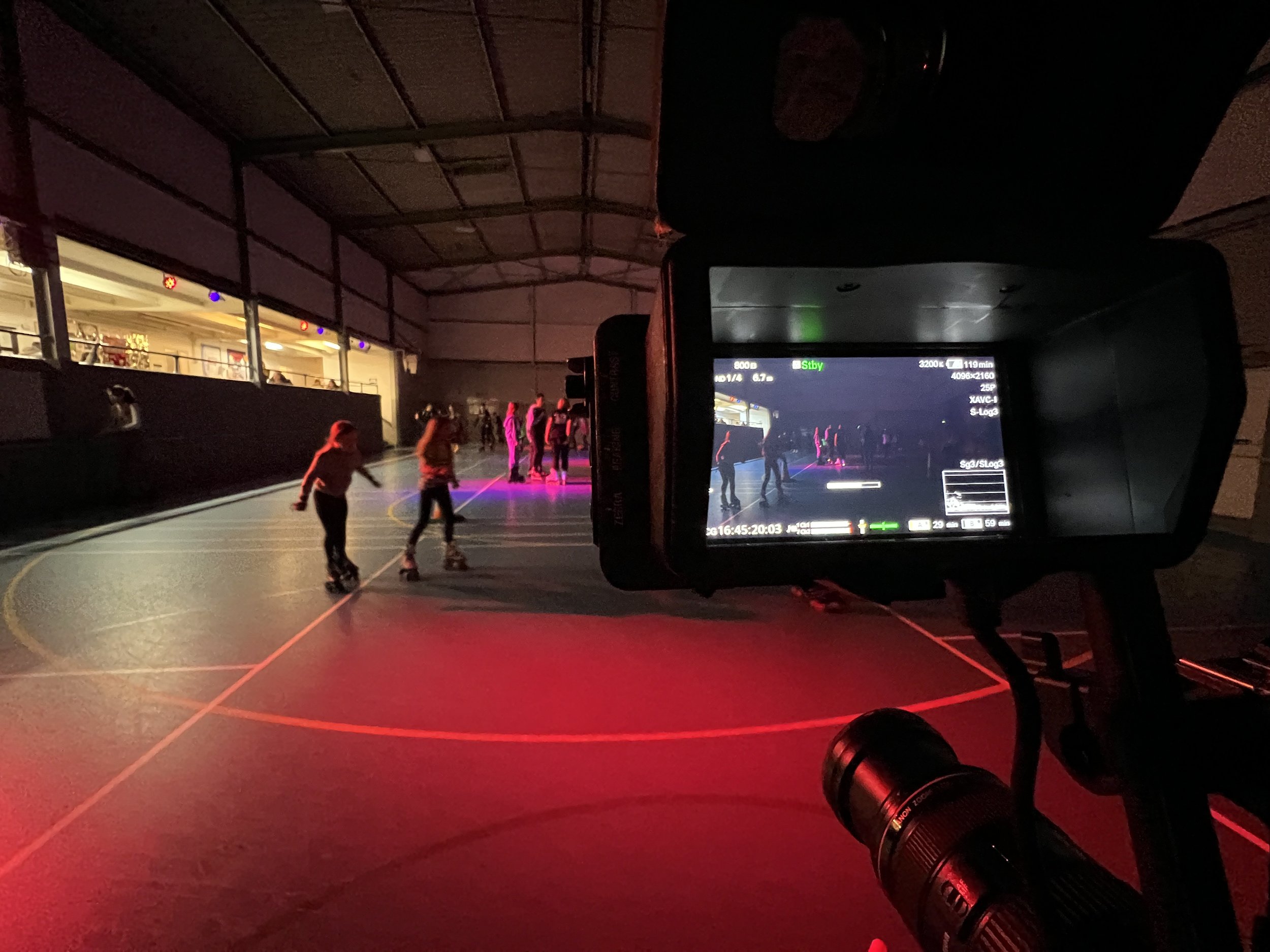 A skating rink in dim light, being filmed. The image shows the camera and the view of the rink on the camera screen