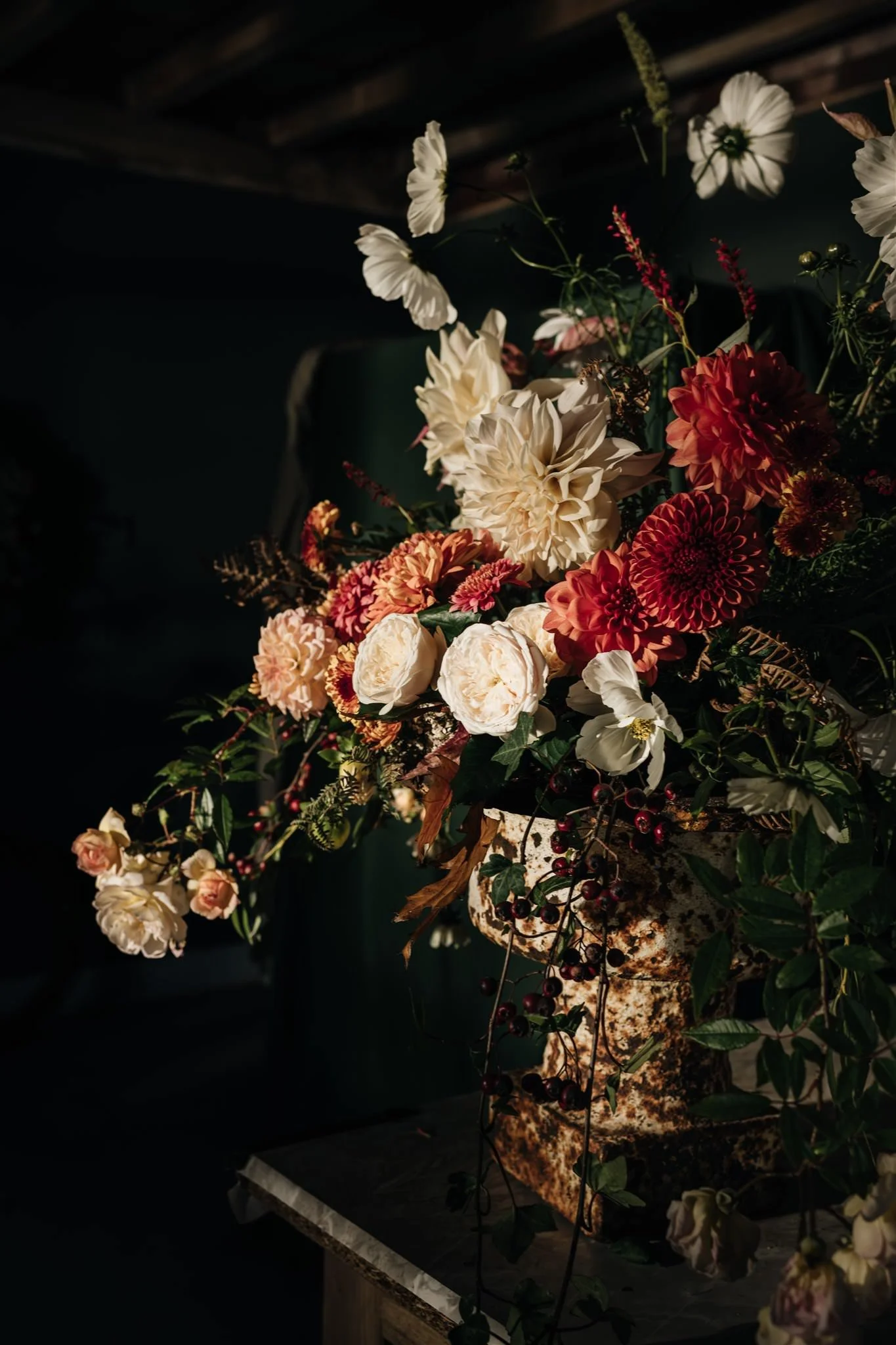 A floral arrangement with white and red flowers in a rustic, speckled stone vase on a table, set against a dark background.