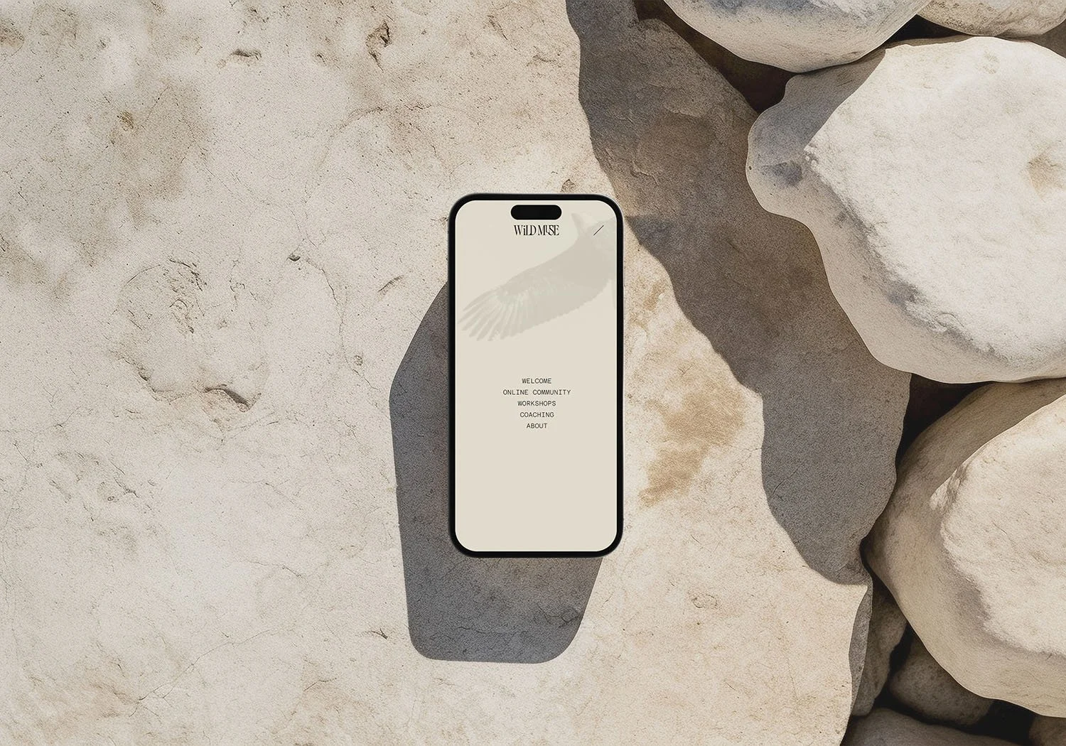 Smartphone placed on sandy ground surrounded by rocks, displaying the WILDMUSE website menu