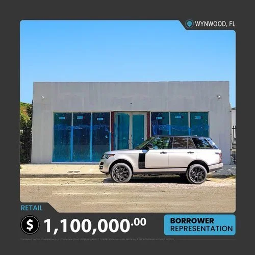 Modern white building with large blue-tinted windows, located in Wynwood, FL. A silver and black SUV is parked in front. Text indicates retail property priced at $1,100,000 with borrower representation.