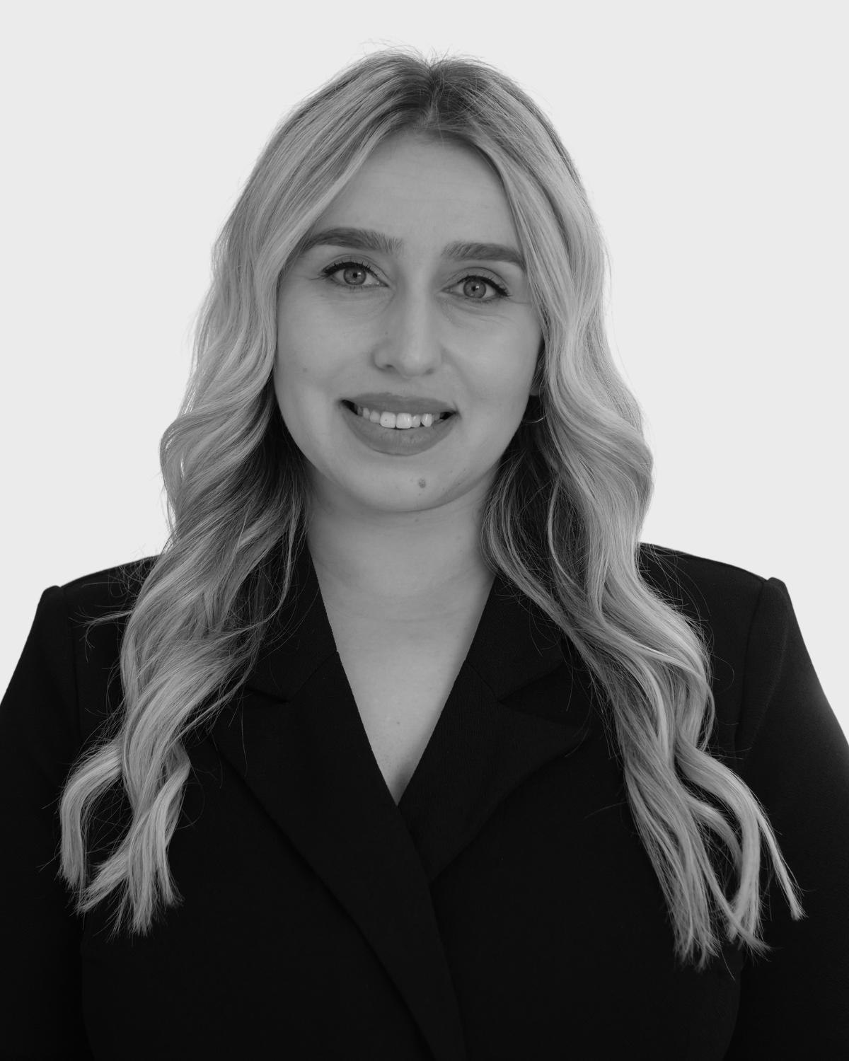 Black and white portrait of a young woman with wavy blonde hair wearing a dark blazer, smiling at the camera.