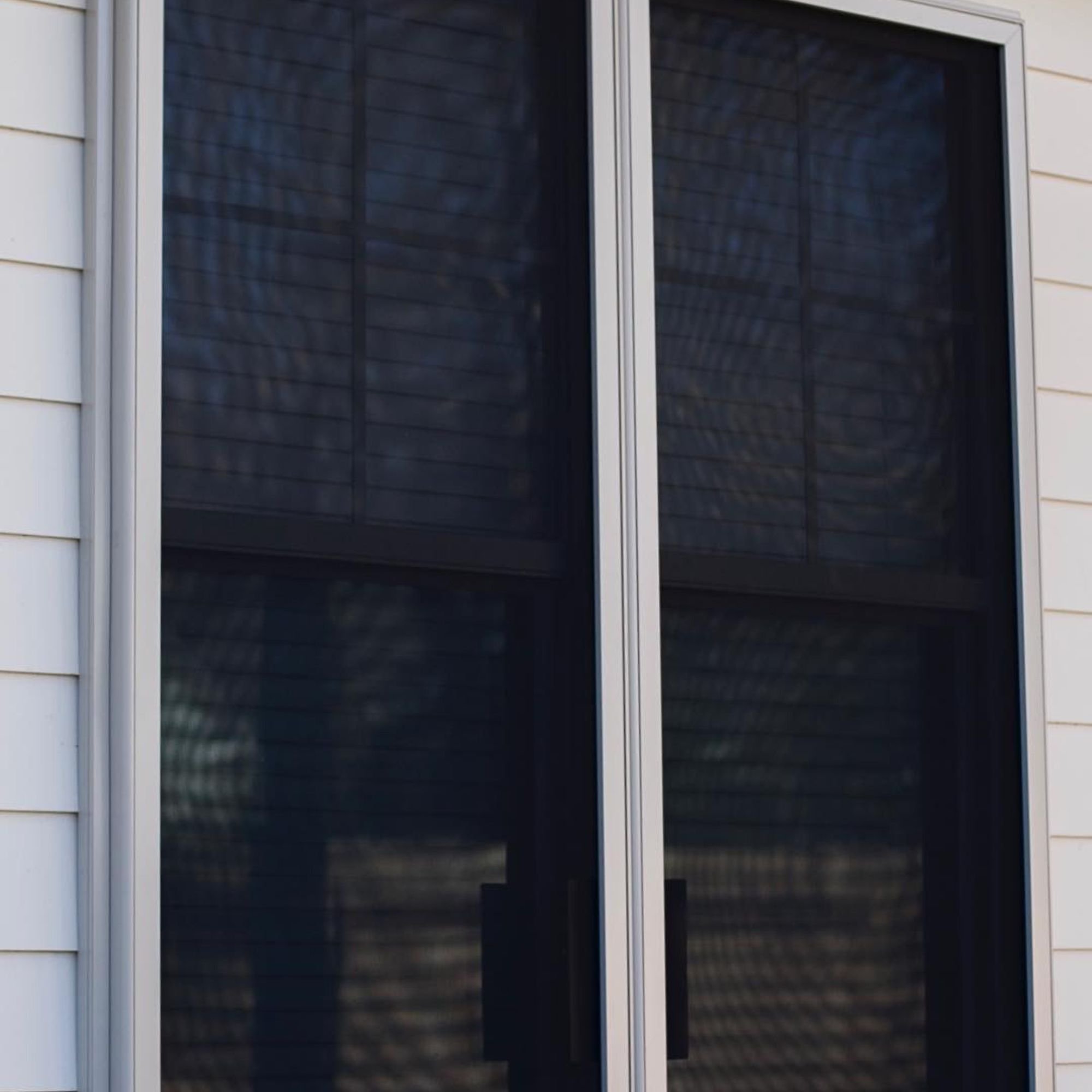 Sliding glass door with mesh screen and visible shadows on the exterior surface.
