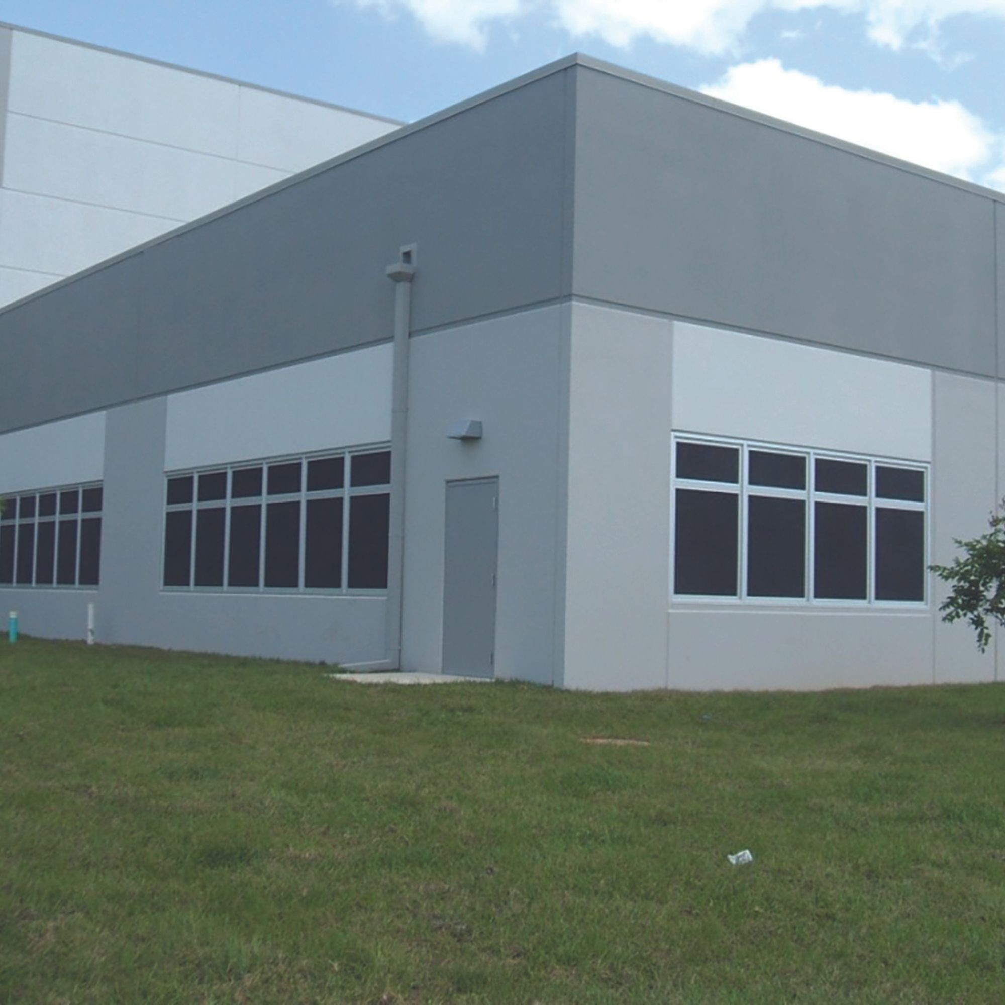 Modern industrial building exterior with large windows and grass lawn