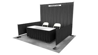 Trade show booth with a black corrugated backdrop, two white chairs, and a small table with a black tablecloth, set on a gray carpet.