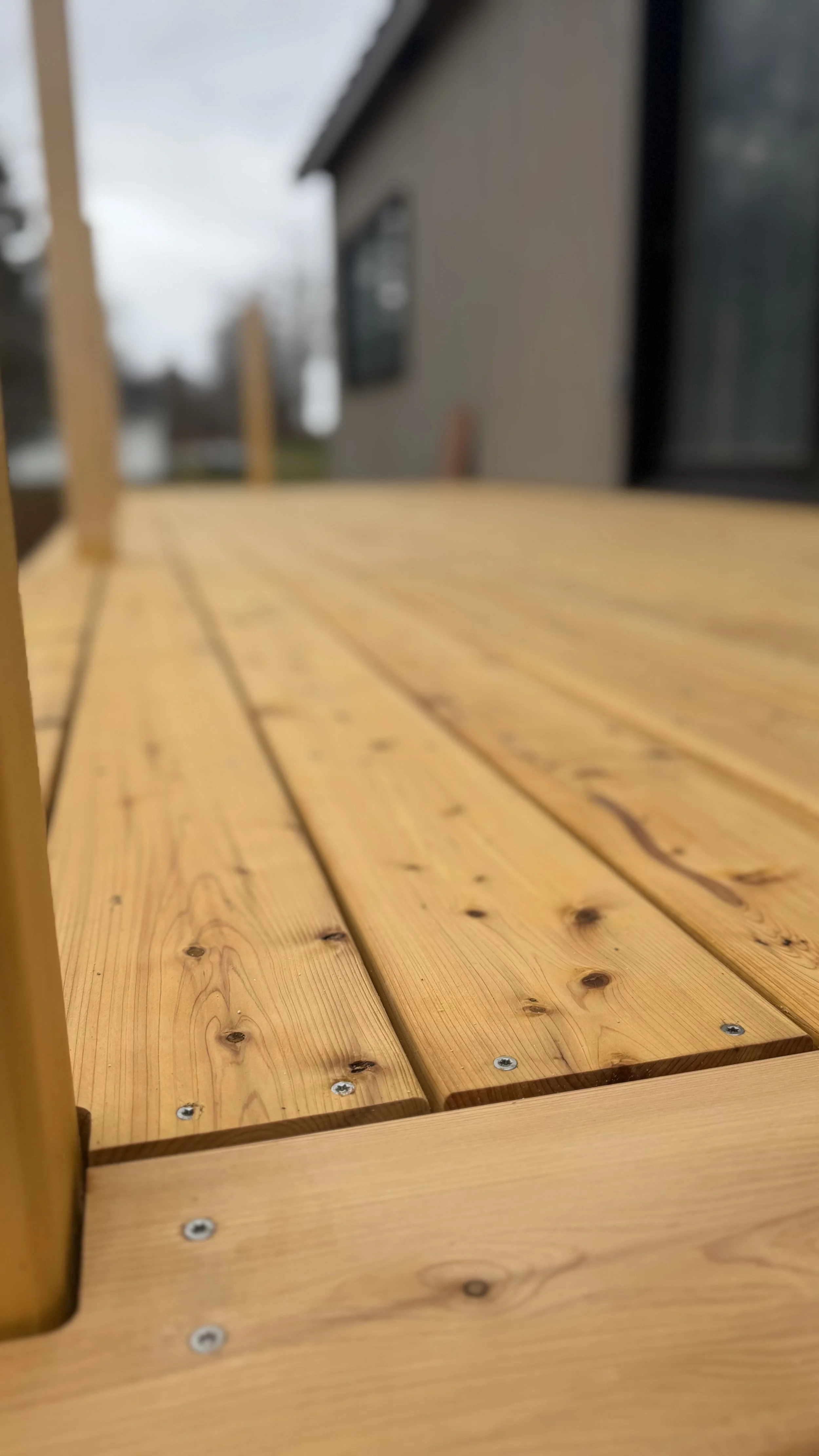 Close-up of a wooden outdoor table with a blurred house and cloudy sky in the background.