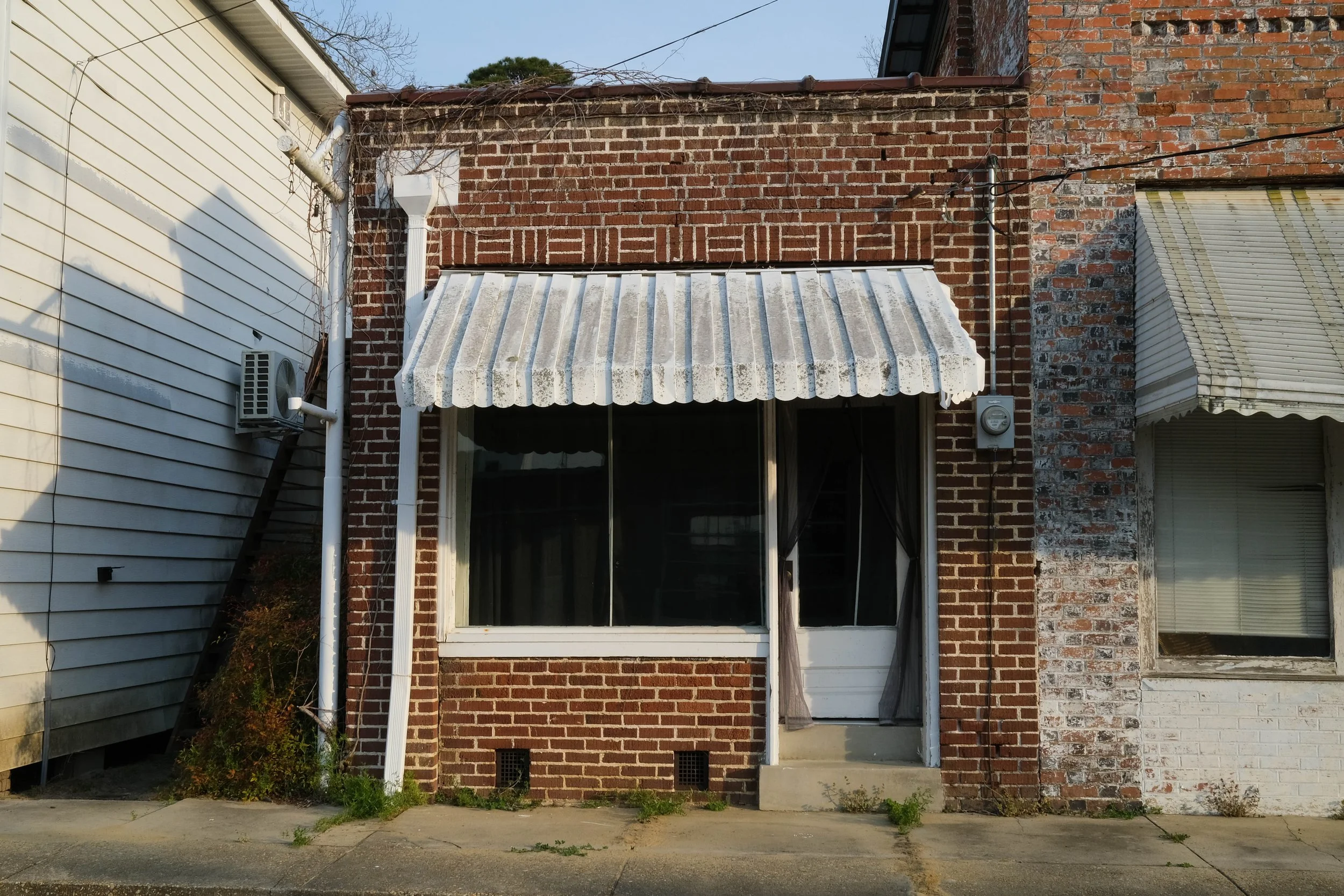 Square brick storefront from 1920s with white metal awning over window in Rose Hill, North Carolina.