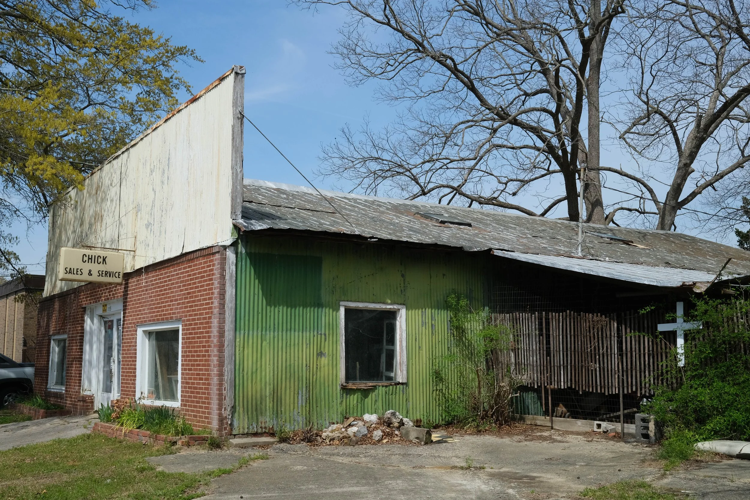 Brick and aluminum siding storefront with sign stating "Chick, Sales and Service." A white cross adorns the fence beside the building. Downtown Fremont, North Carolina.