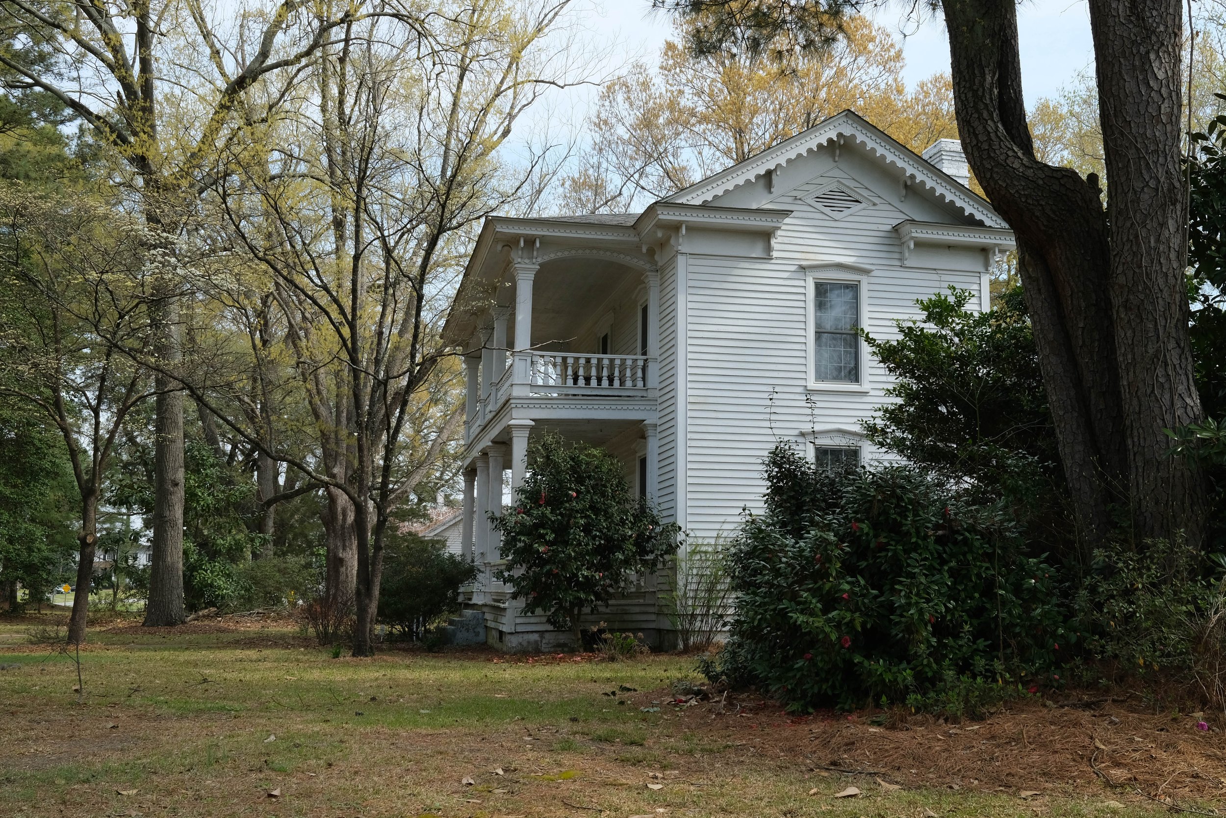 Antebellum two story home with white clapboard trim and double porches in sandy yard with pine trees and azalea bushes. Faison, North Carolina.