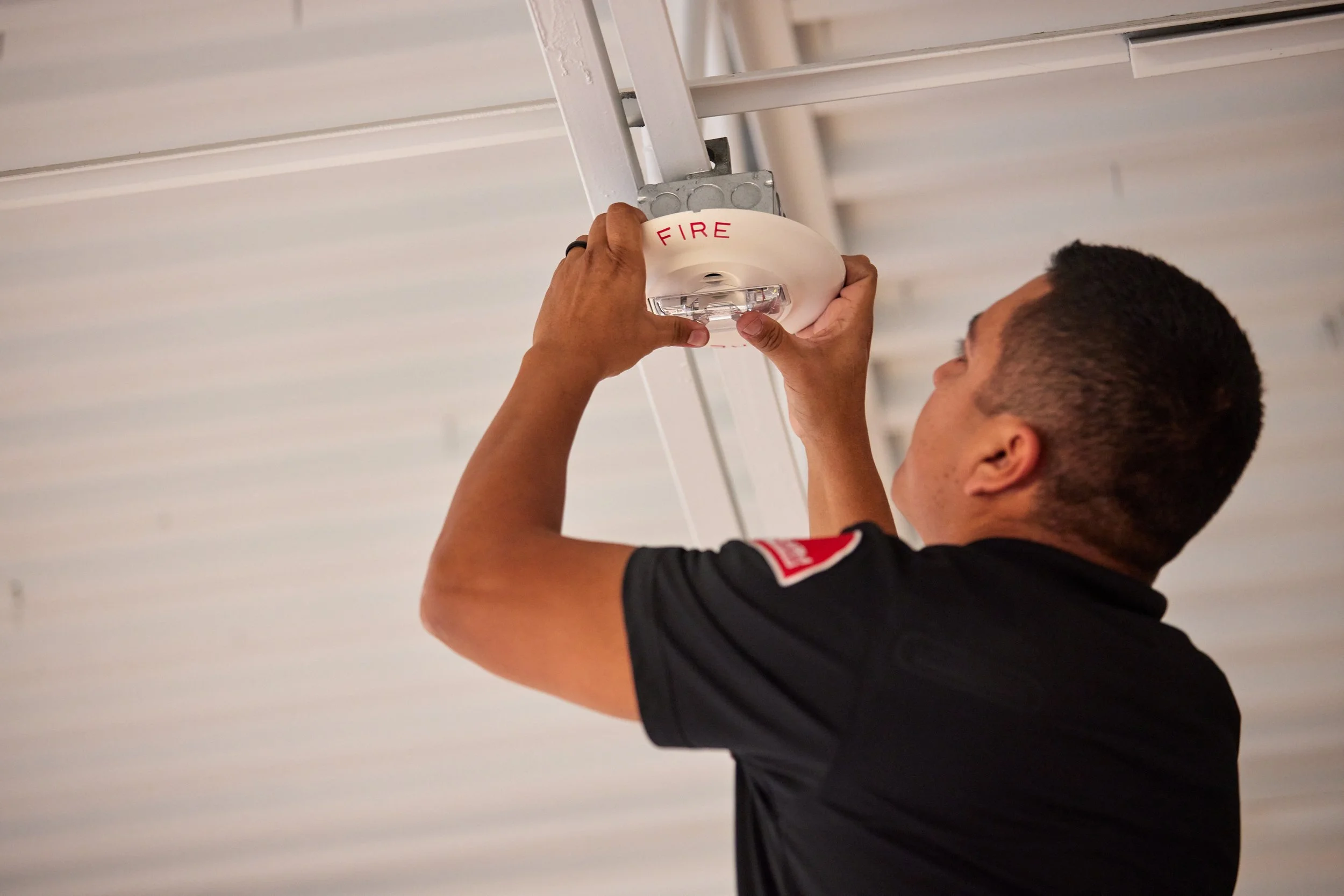 SecurAlarm Technician servicing a fire horn/strobe on the ceiling
