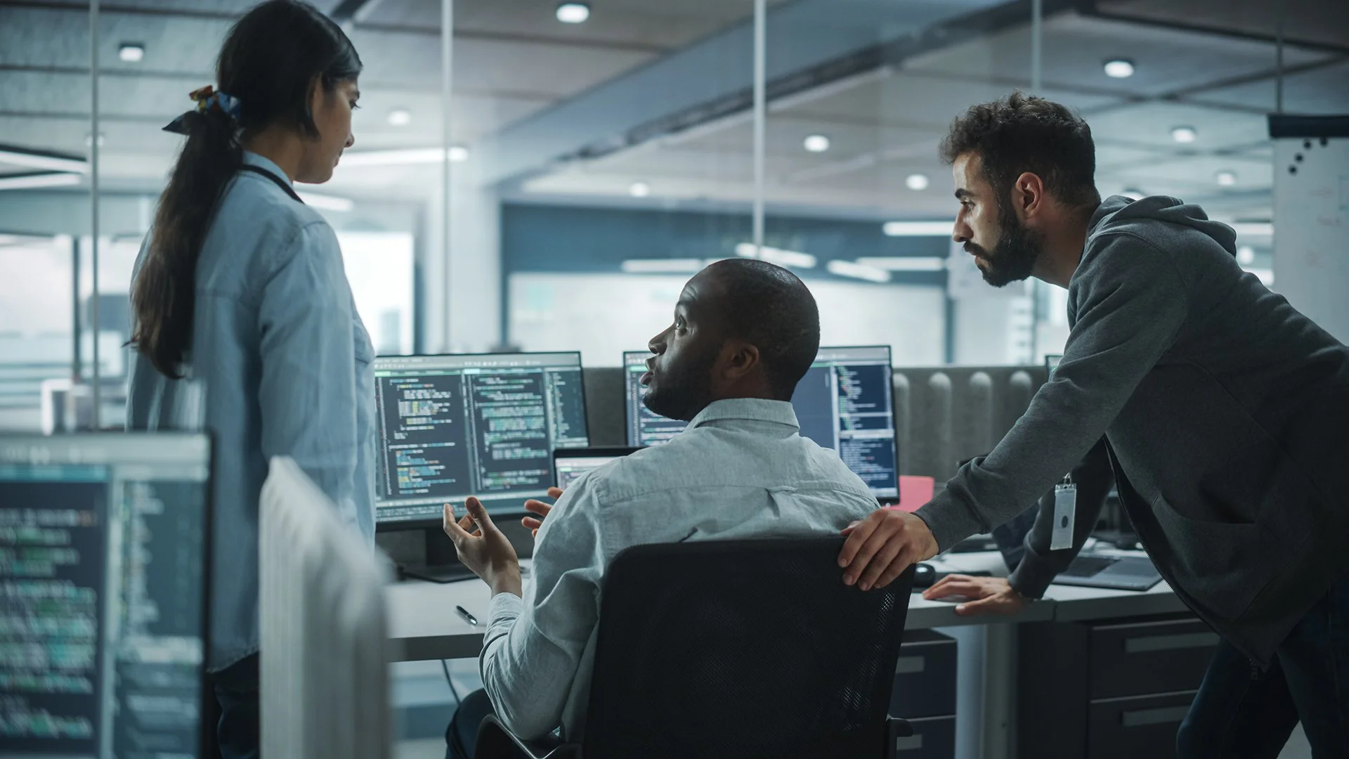 Three confused coworkers looking over multiple computer monitors