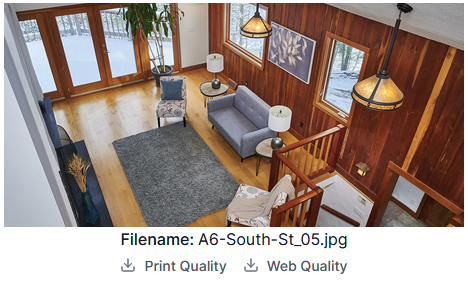 Living room with wooden walls, a gray sofa, a patterned armchair, a coffee table, two table lamps, and large windows showing a snowy outdoor scene.