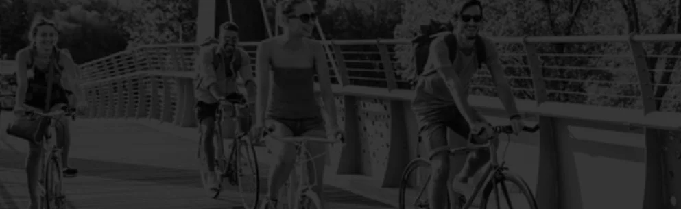 Four people riding bikes on a bridge with railing, smiling and wearing casual clothing.