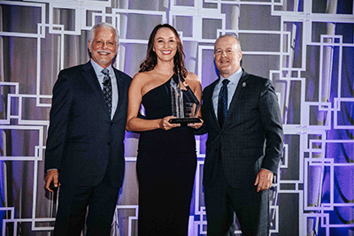 Two men surrounding a woman holding an award