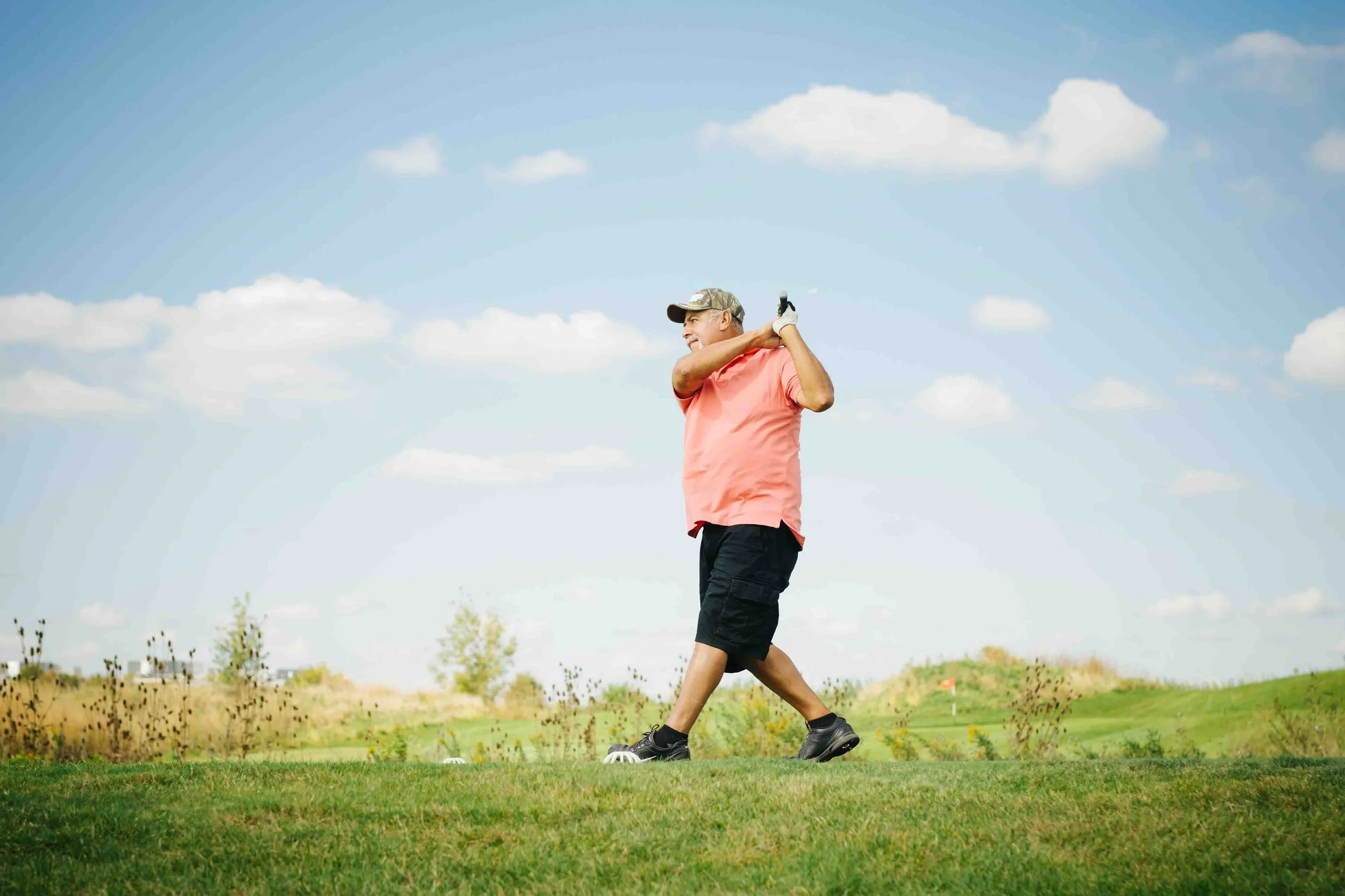 Man in golf attire who just hit golf ball gazing.