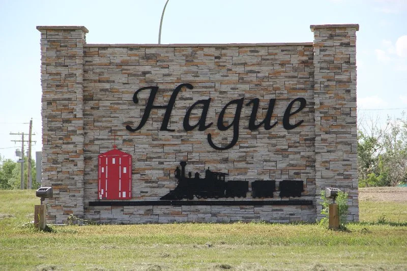 A brick wall with the word 'Hague' written in black cursive letters, a silhouette of a steam locomotive, and a red barn symbol.