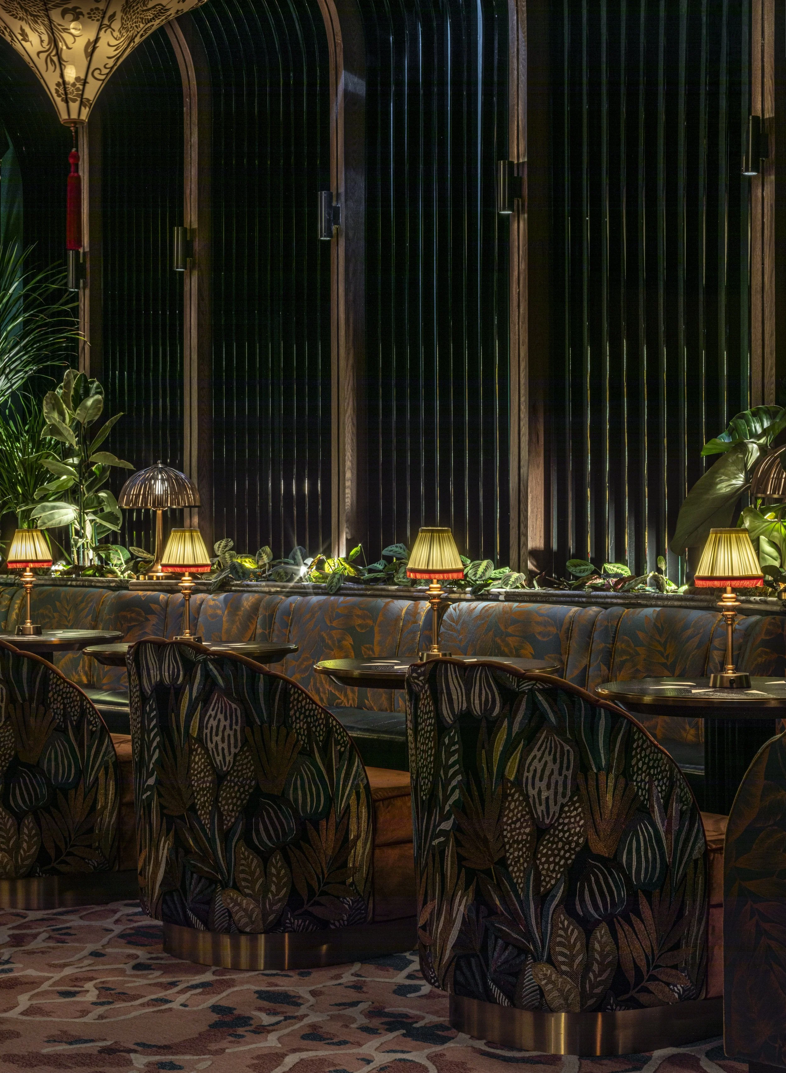 A close up view of the sky lounge. The armchairs have a scalloped top edge and are backed in bold colourful natural patterned fabric by Casamance. Banquette with silky palm pattern fabric. Birdcage slats behind.