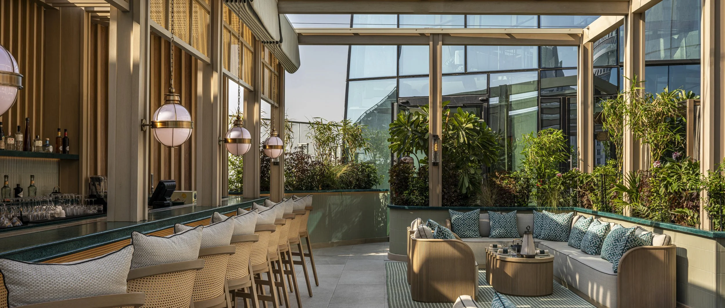 A wide angle view of the Tattu Sky Pool bar. Pool bar to the left hand side has rattan backed bar stools and lanterns. The right hand side is a lounge group with throw pillows.