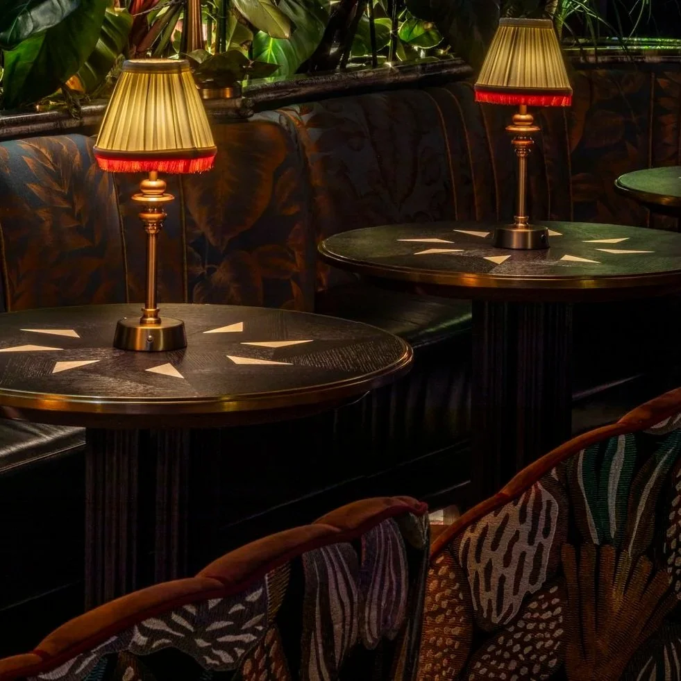 Close up of the cocktail tabls with two toned veneer insets in triangle graphic. The scalloped armchairs in the foreground with bold colourful natural pattern..
