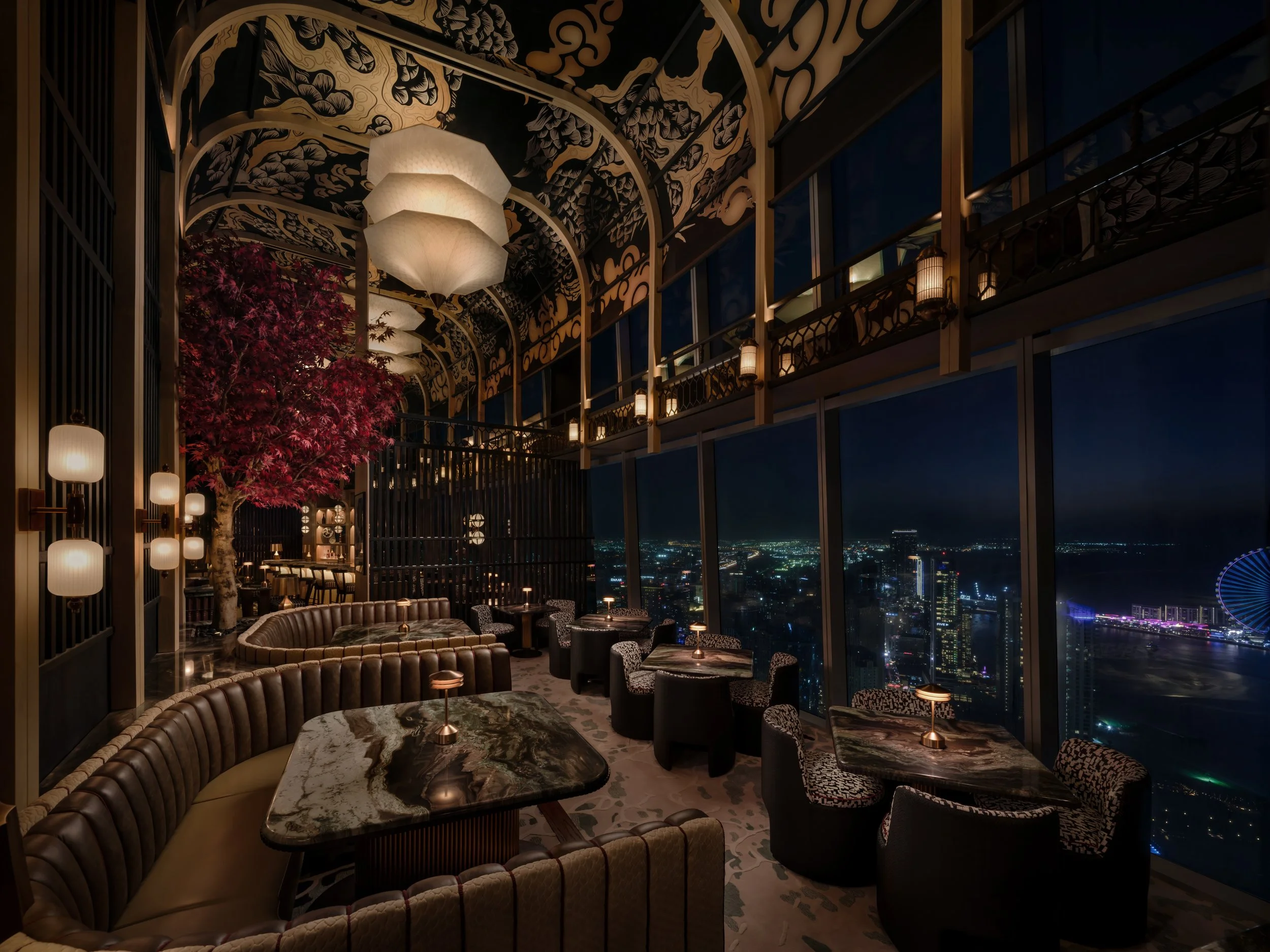 An image of the white dragon bar at night time at Tattu Dubai. The vaulted dragon graphic ceiling is triple height, with oversized 3D printed penants hanging below. 