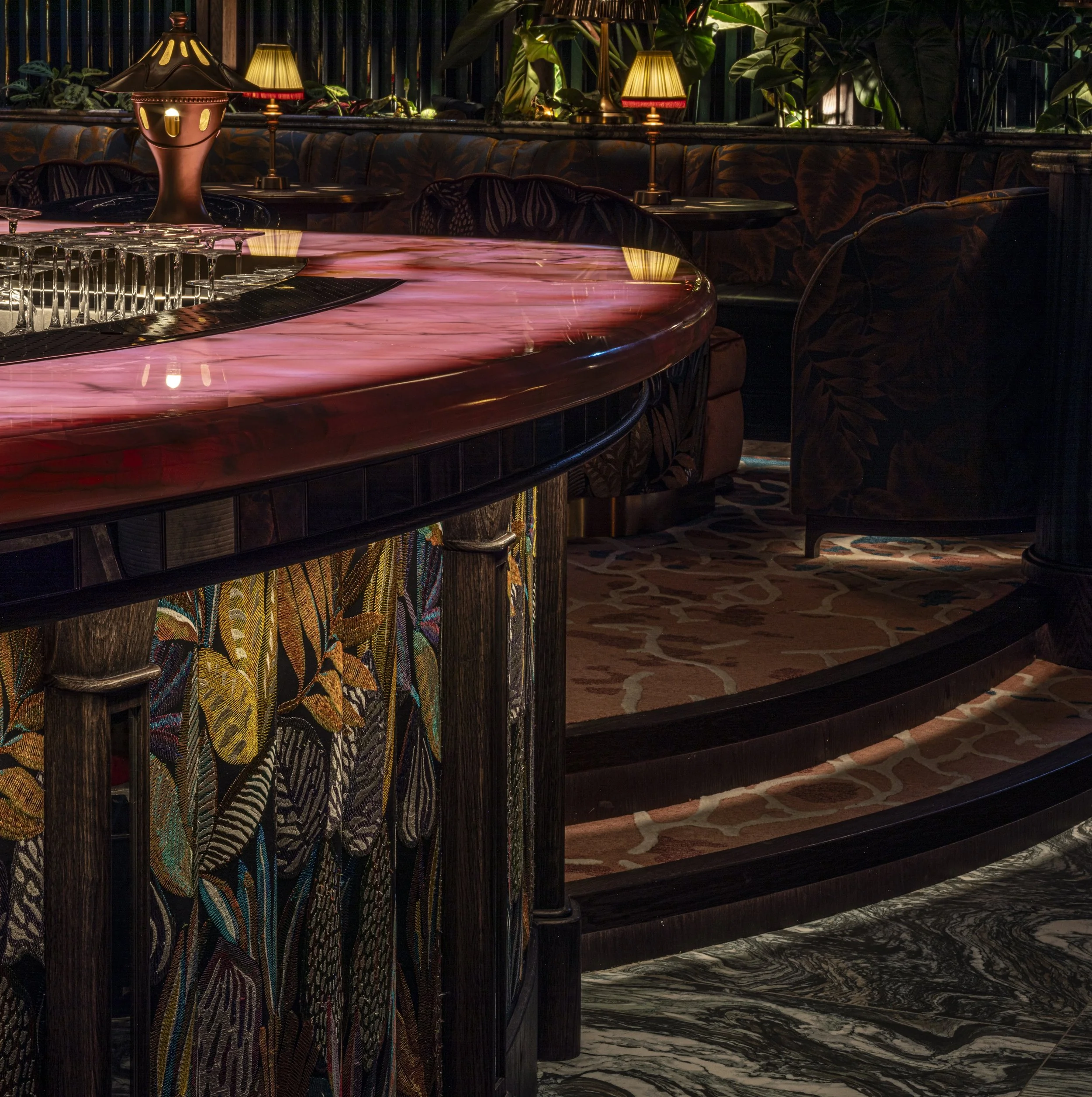 Close up of the glowing pink onyx bar counter. Mirror pieces below. The front bar is a bold graphic natural pattern by Casamance. Golden cermaic table lights sit on the bar top.