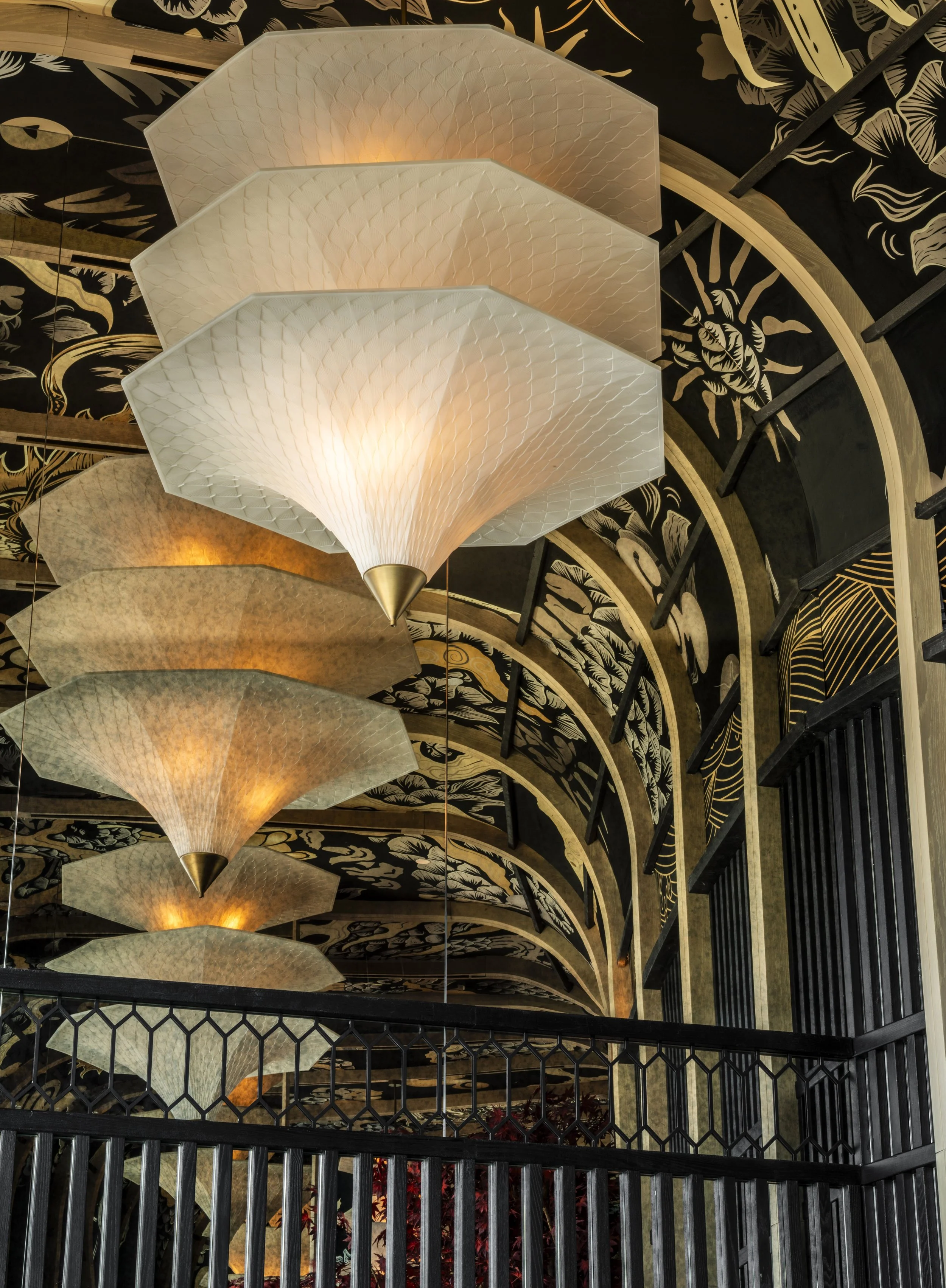 A 3D printed three-tiered pendant with a dragon scale motif. The ceiling behind is a vaulted ceiling in a dragon print fabric. Mirror reflects the pendnat back on itself multiple times.