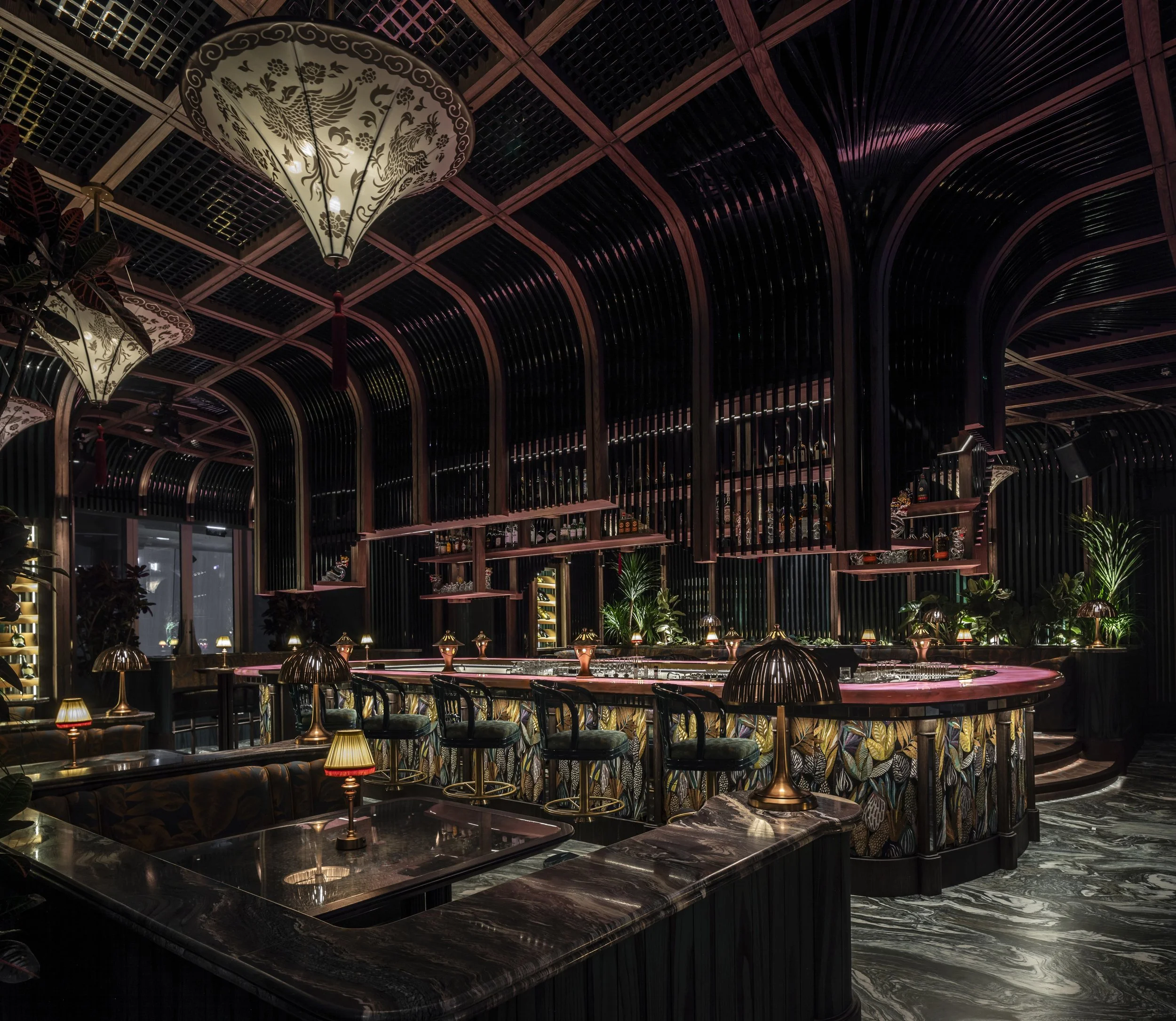 The phoenix bar at Tattu Sky Lounge. A ceiling inspired by a birdcage sweep up and over the central bar, which is a glowing pink onyx countered bar. 