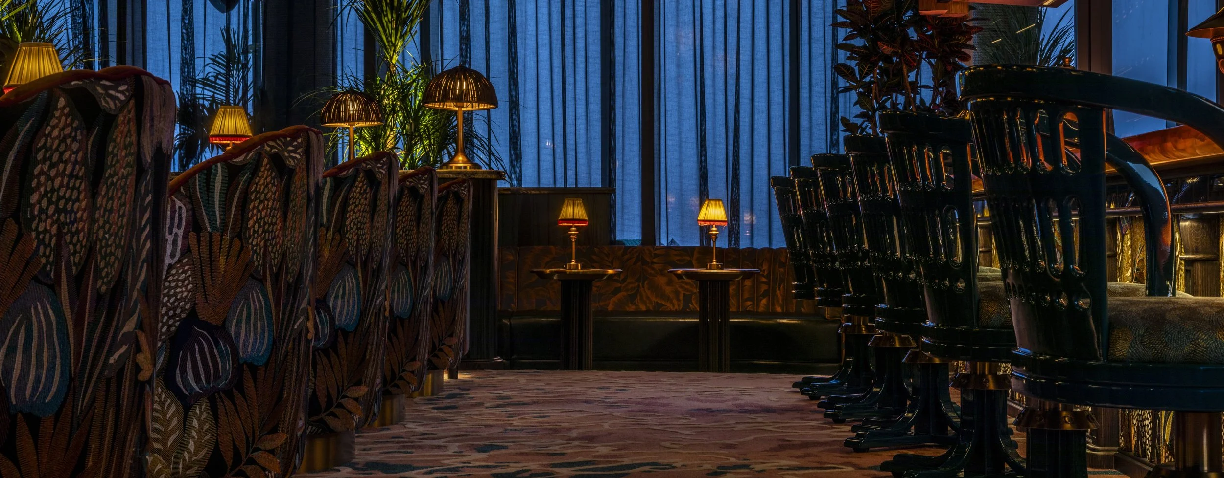 Close up of the low bar stools opposite the lounge chairs. The fabirc on the front bar matches the fabric on the back of the lounge chairs. Vibrant bold patterning of foliage. High gloss turquoise lacquer barstools.