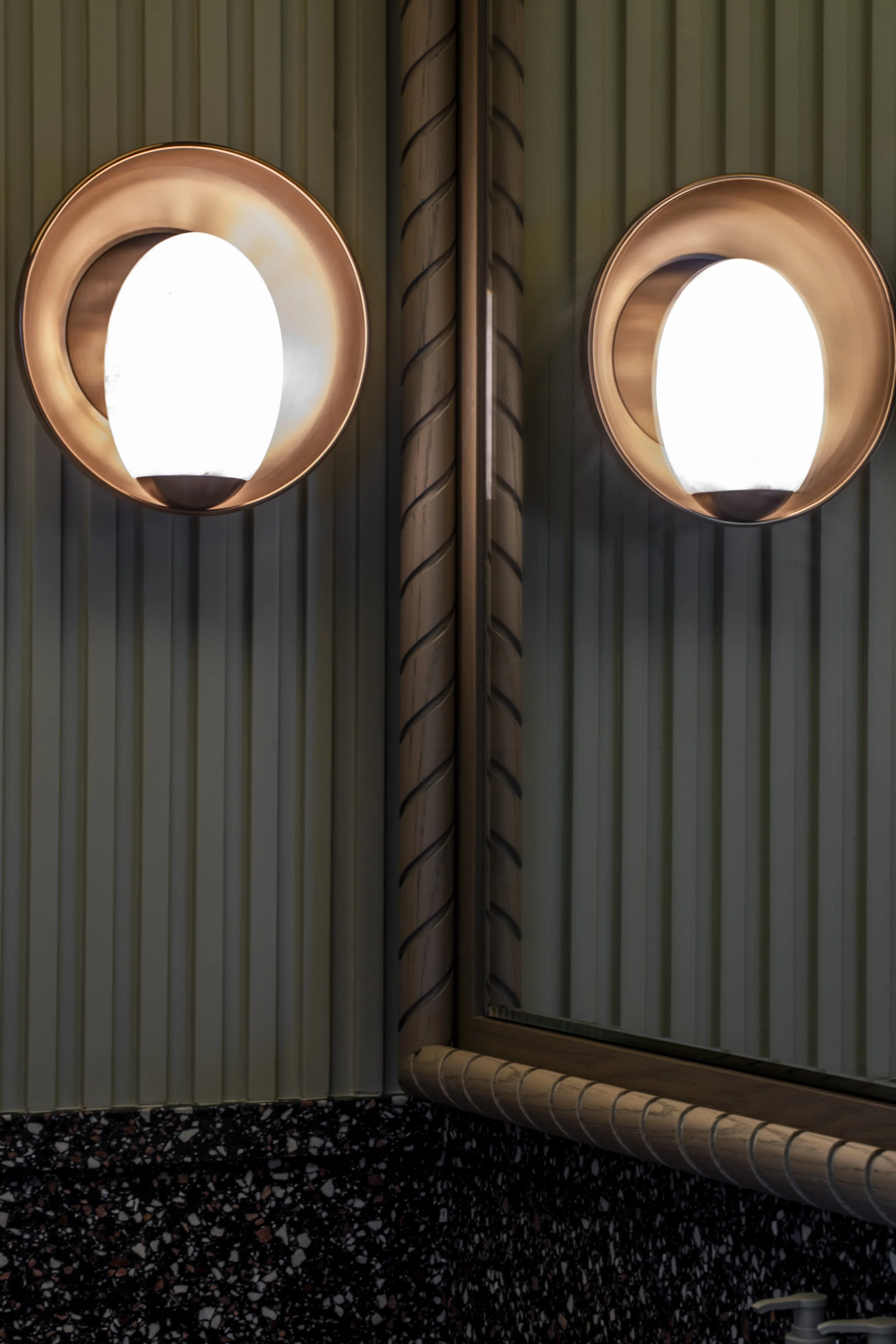 A close up view of the restrooms with a hand turned timber mirror and a custom wall sconce.